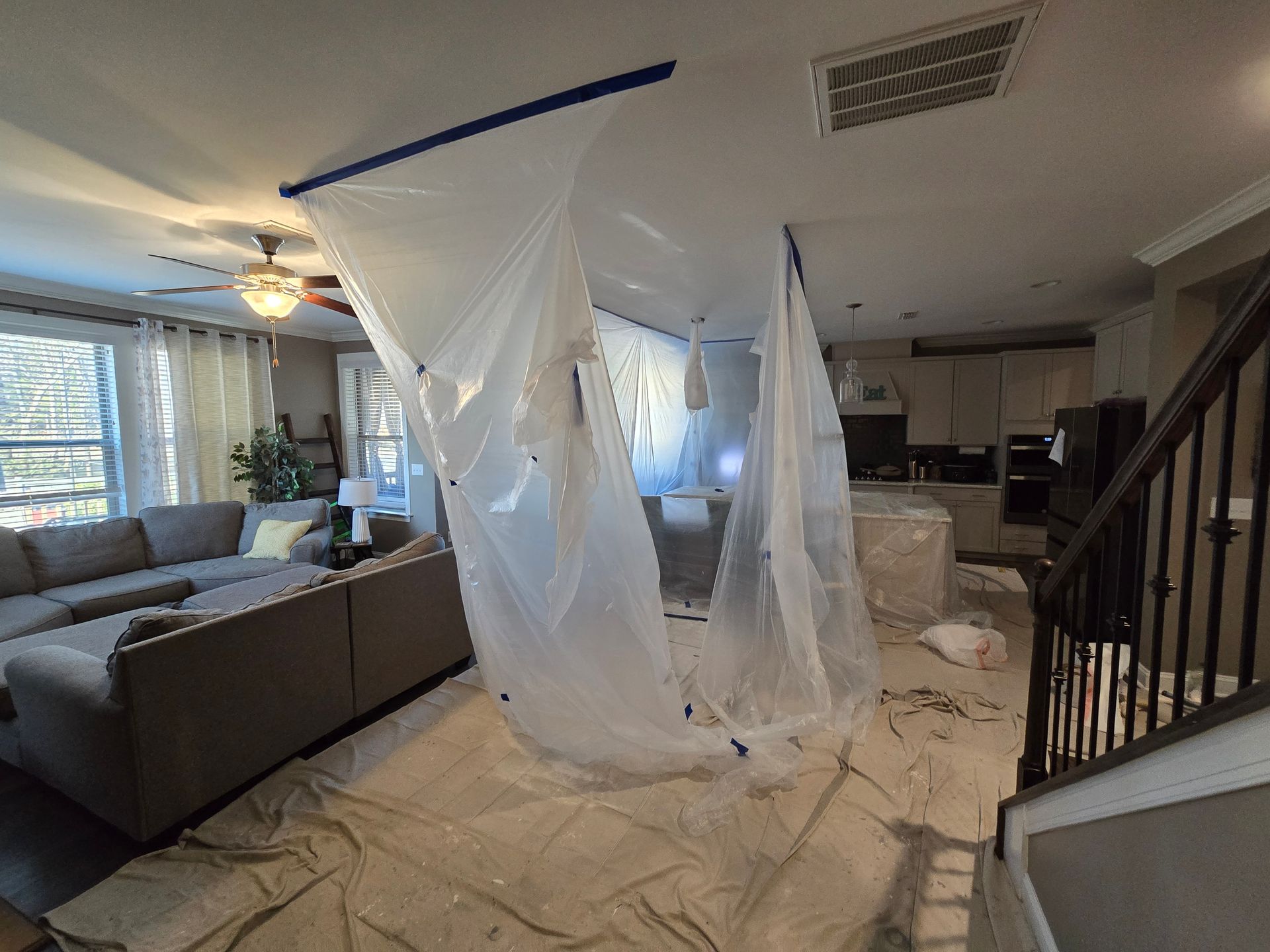 Living room covered in plastic sheeting, with a tarp-draped ceiling and scattered debris during renovation