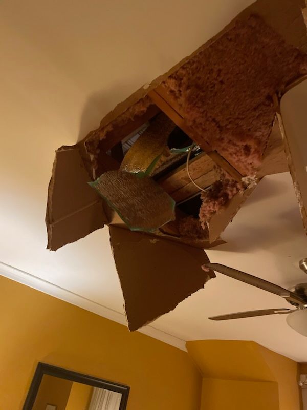 Ceiling hole with exposed insulation and hanging panels in a yellow room, near a ceiling fan.
