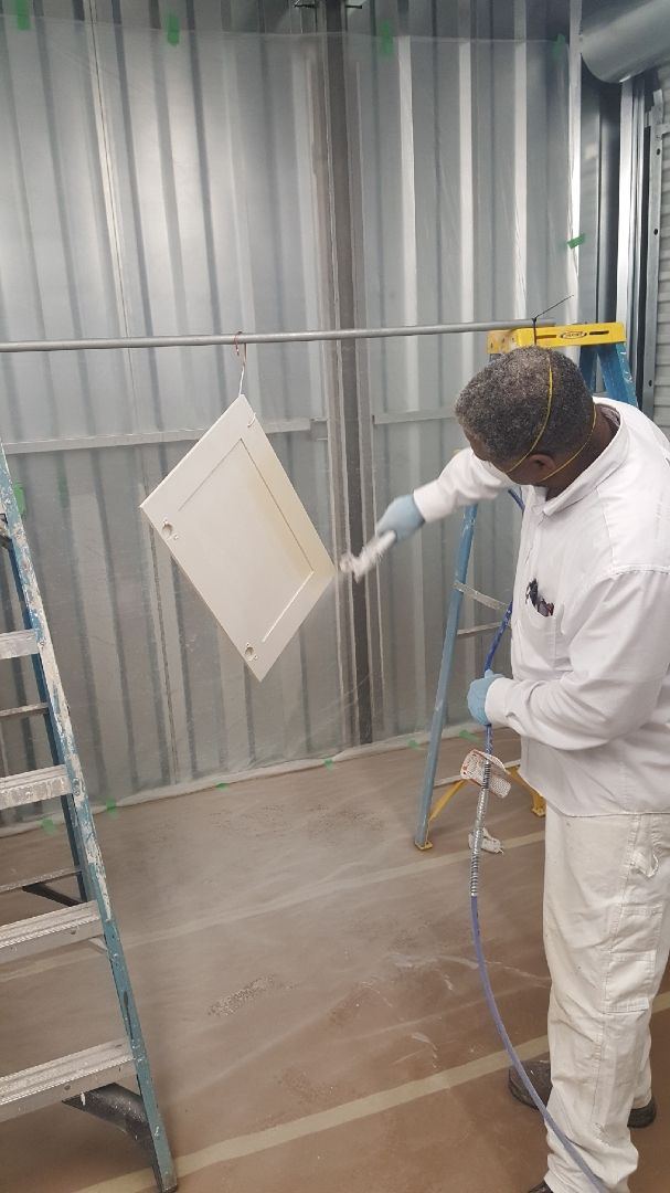 Worker spray-painting a white panel inside a metal-walled industrial booth