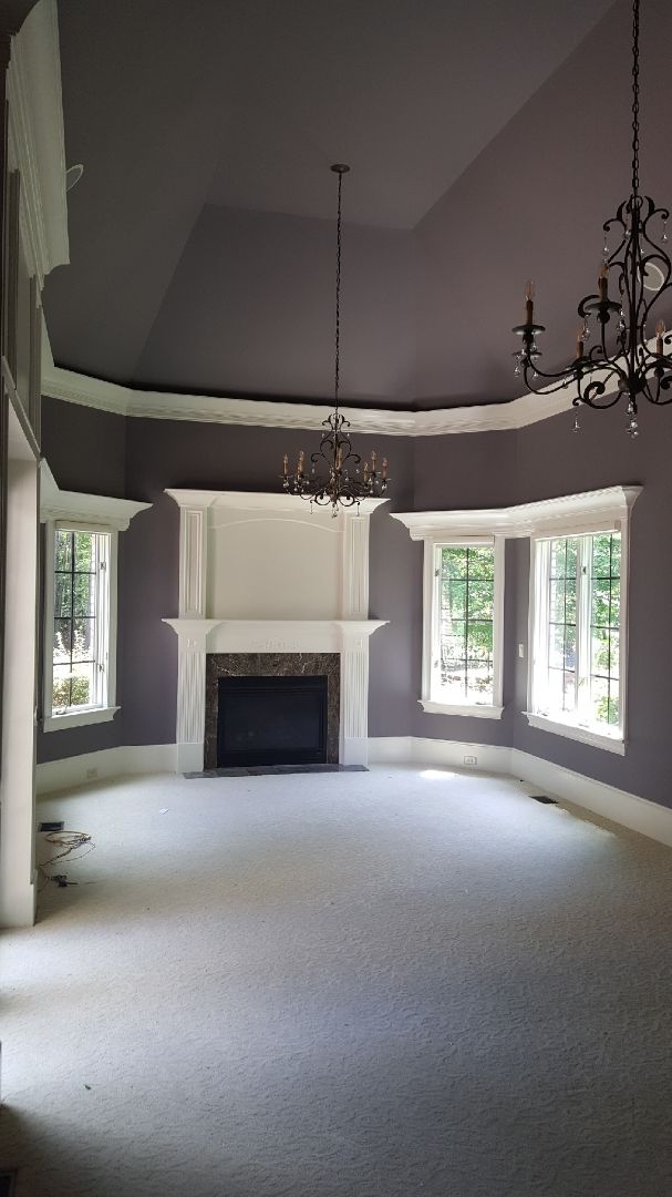 Elegant empty living room with white fireplace, gray walls, chandeliers, and tall windows