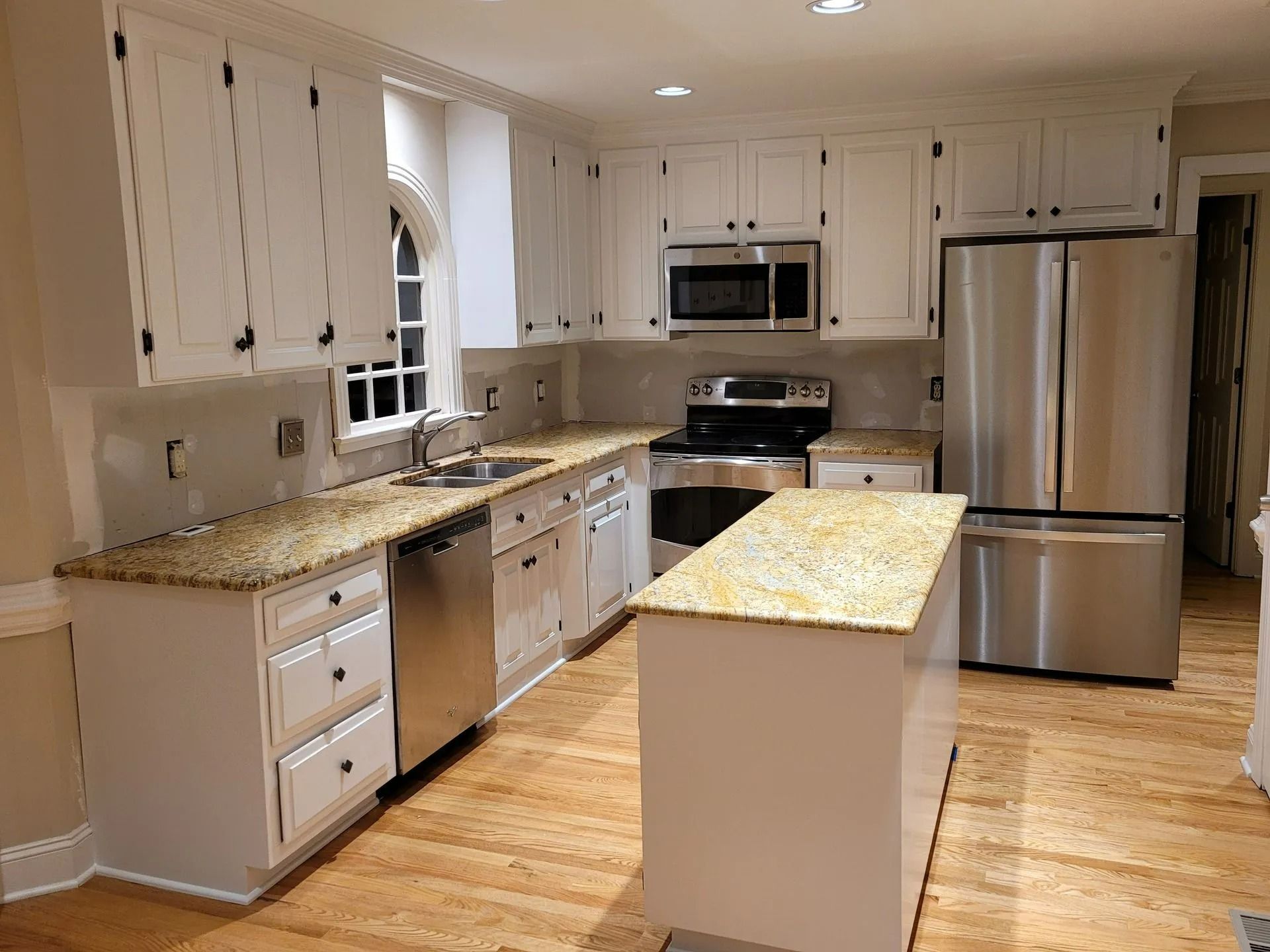 Bright kitchen with white cabinets, granite countertops, stainless steel appliances, and a center island on hardwood floors