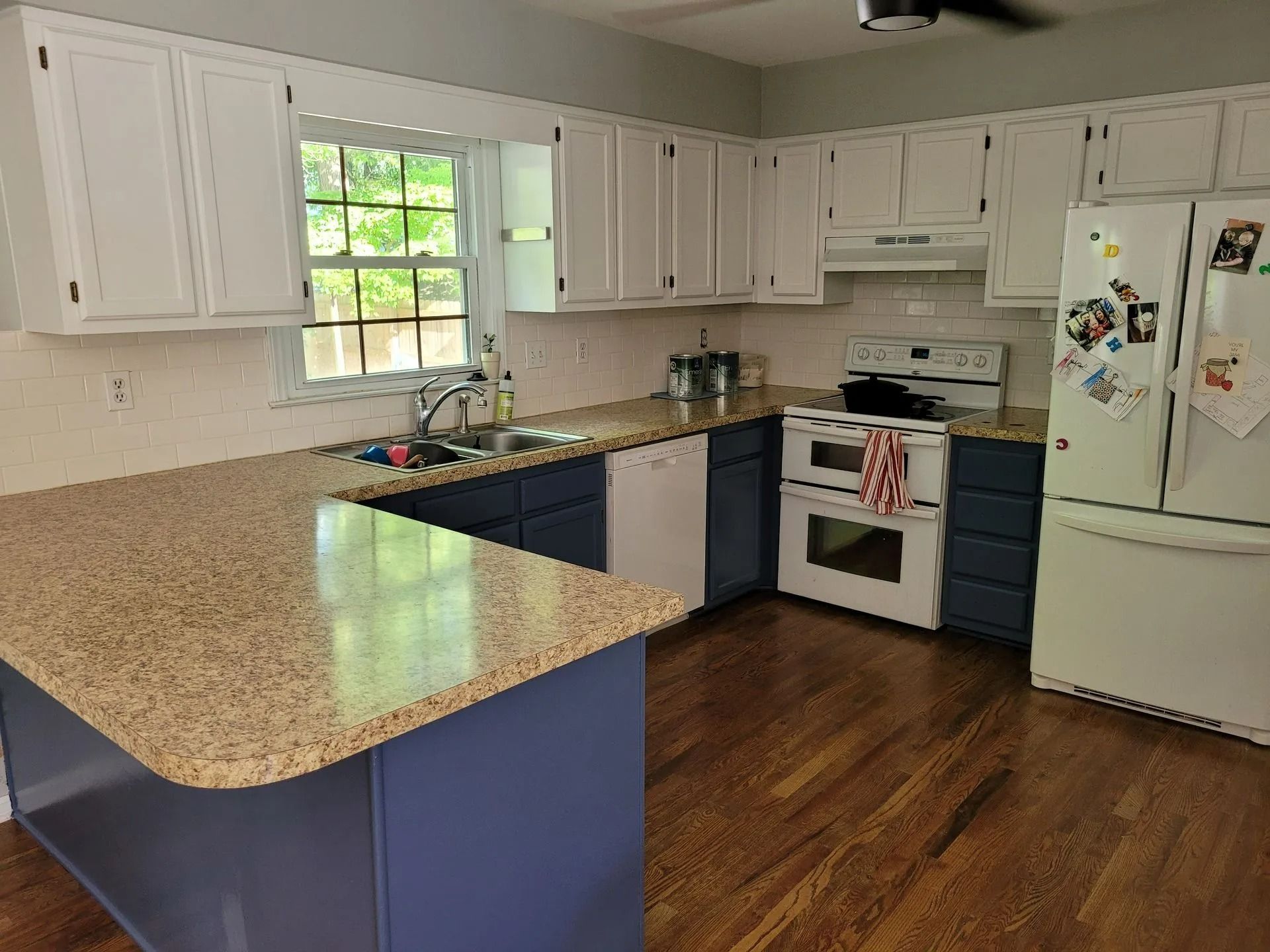 Bright kitchen with white cabinets, blue island, speckled countertop, wood floor, and white refrigerator