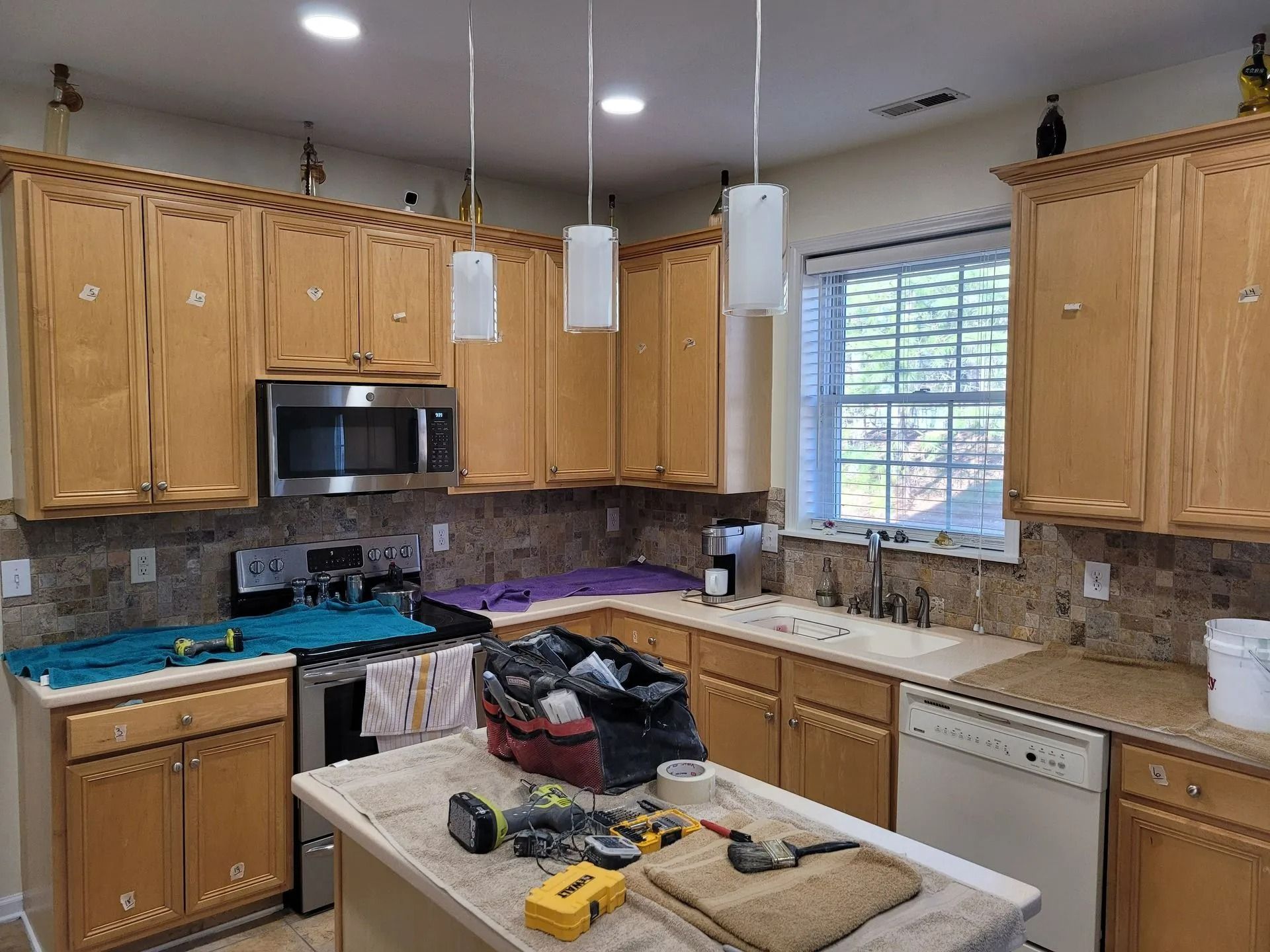 Messy kitchen with wood cabinets, island tools, and a dishwasher under a window