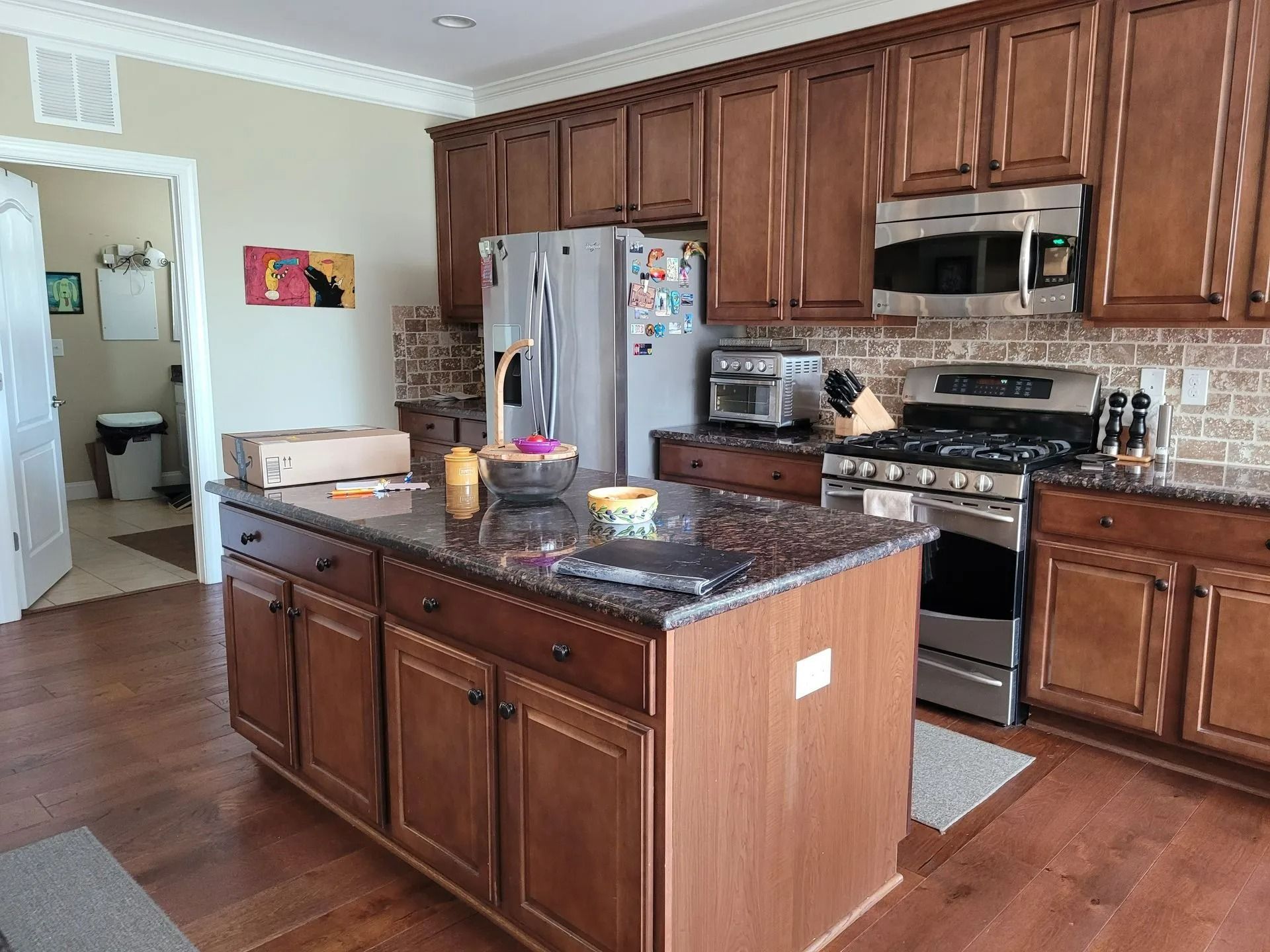 Bright kitchen with wood cabinets, granite island, stainless appliances, and hardwood floors.