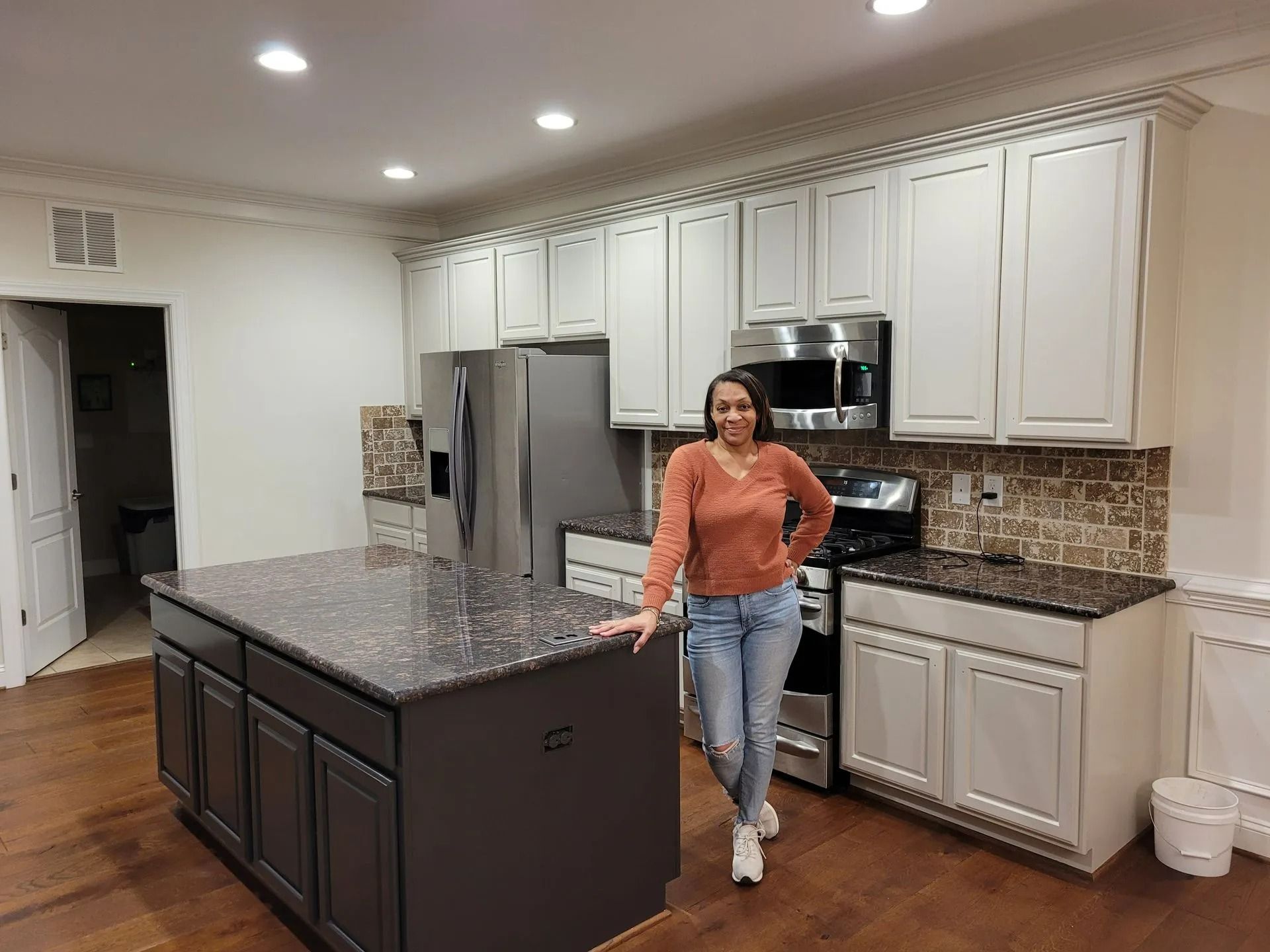 Woman standing in a modern kitchen beside a large island and stainless steel appliances