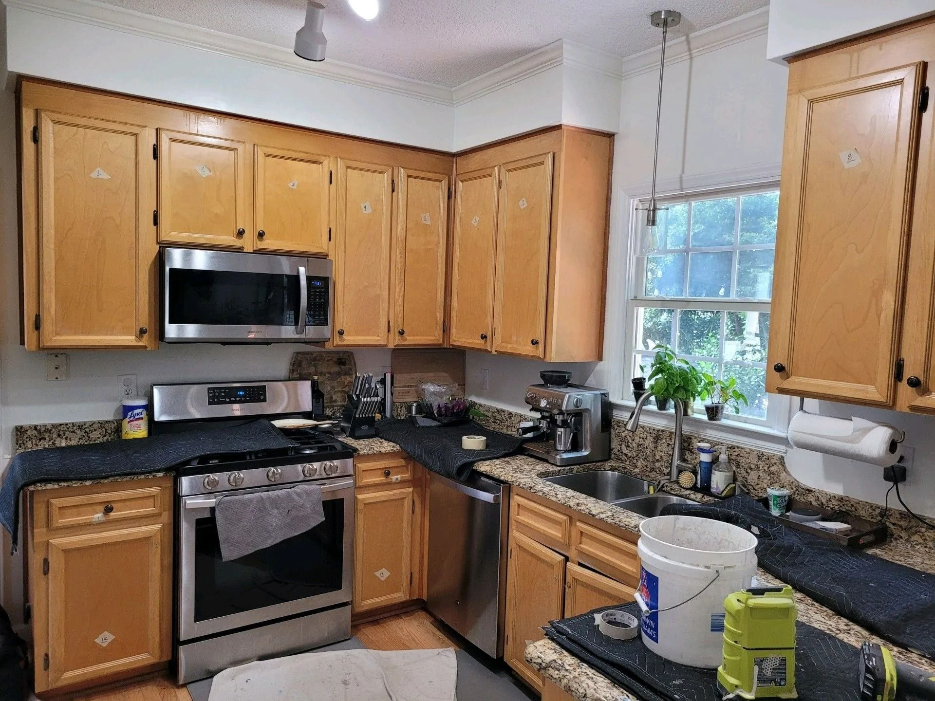 kitchen with wooden cabinets, stainless steel stove and microwave, sink by a window, and cleaning supplies on the counter.