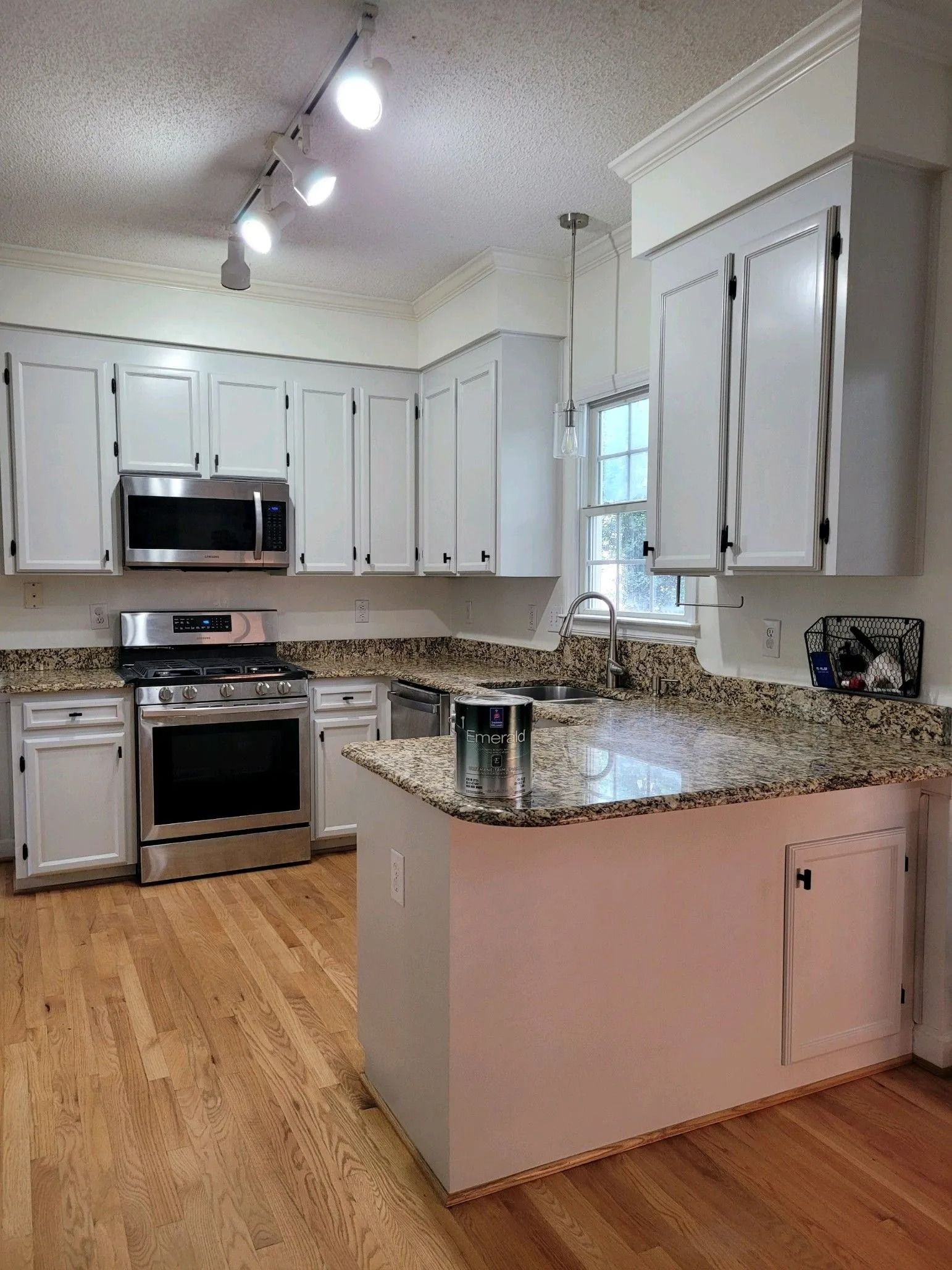 Modern kitchen with white cabinets, granite island, stainless appliances, and hardwood floors.