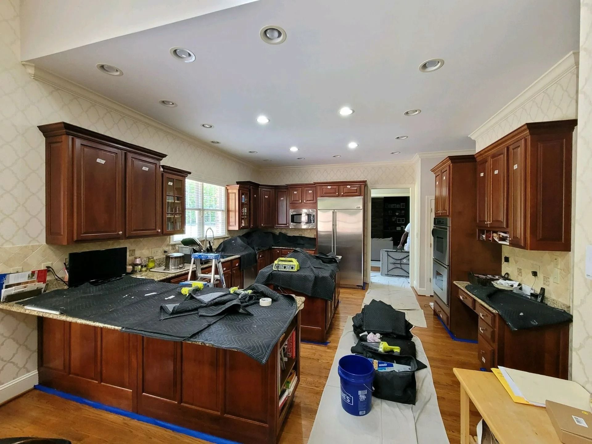 Cluttered kitchen with dark wood cabinets, black countertops, and cleaning supplies on the floor