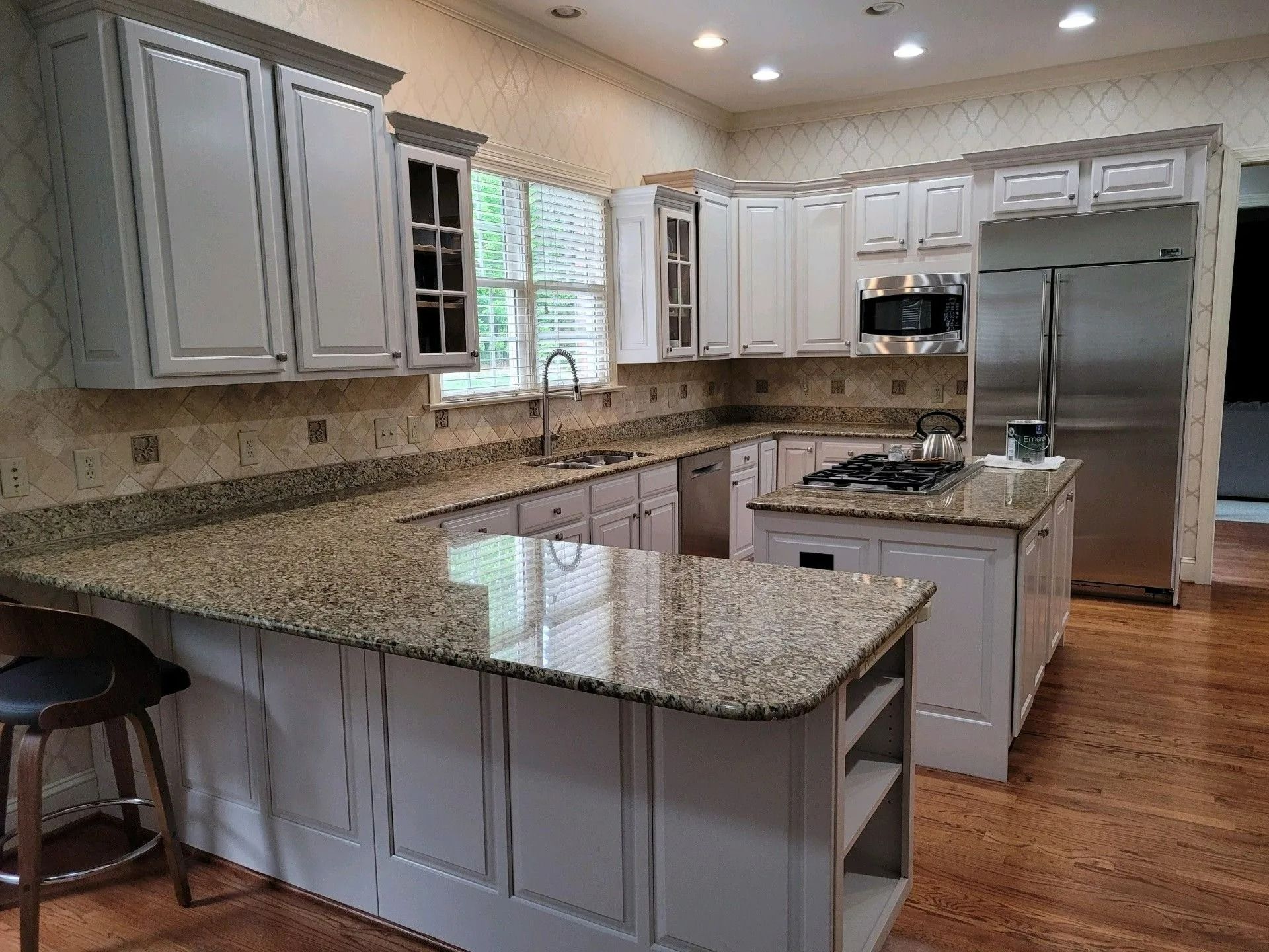 Bright kitchen with white cabinets, granite countertops, island, stainless steel appliances, and hardwood floors