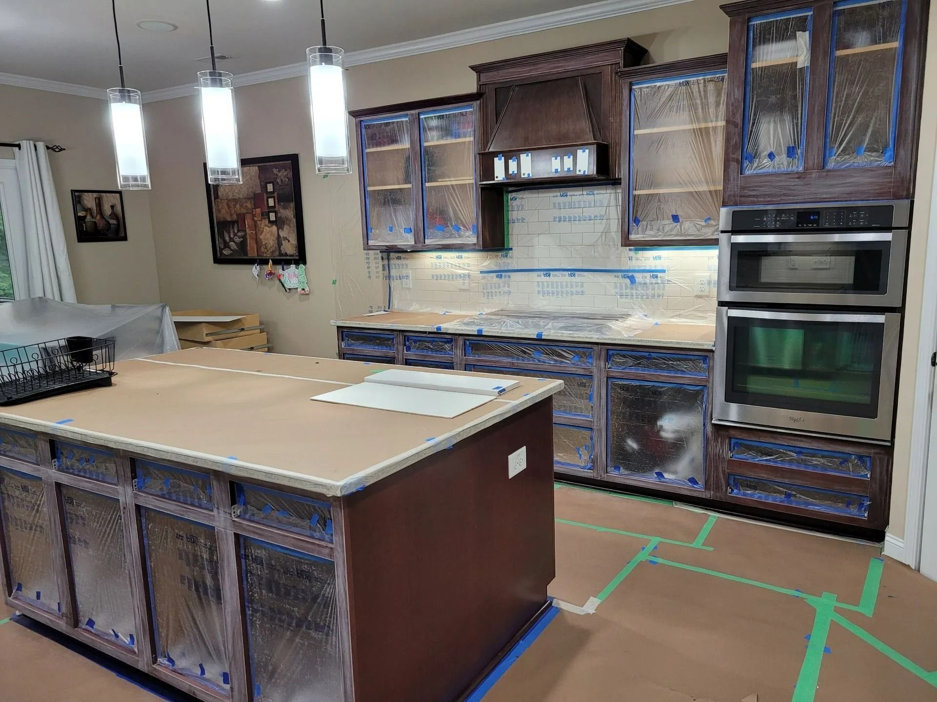 Unfinished kitchen with island, wood cabinets, built-in ovens, and pendant lights.