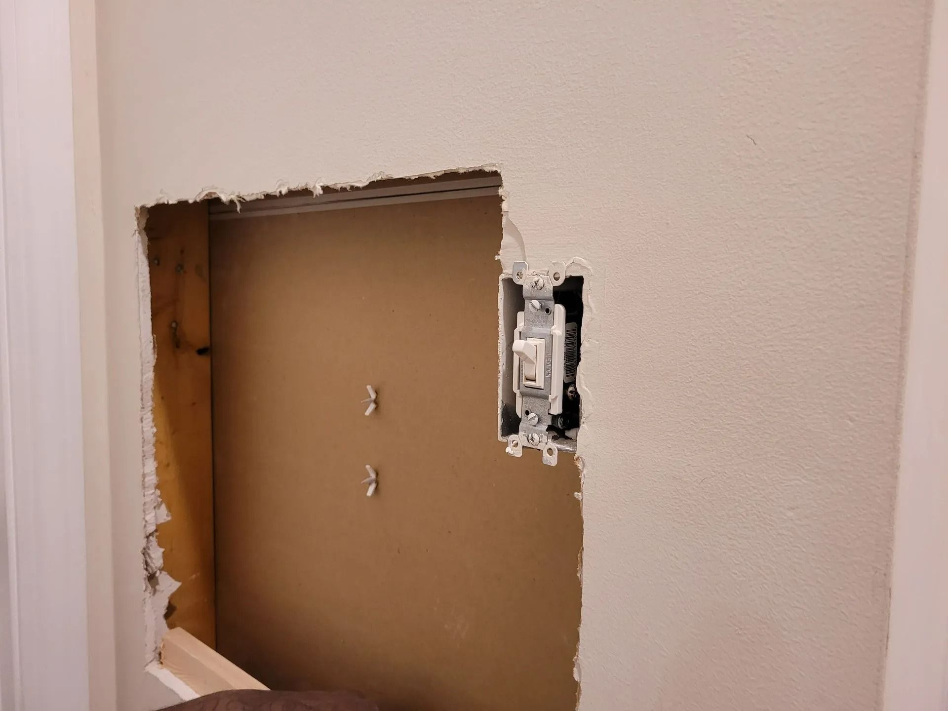 Wall cutout exposing brown drywall with a light switch installed beside it