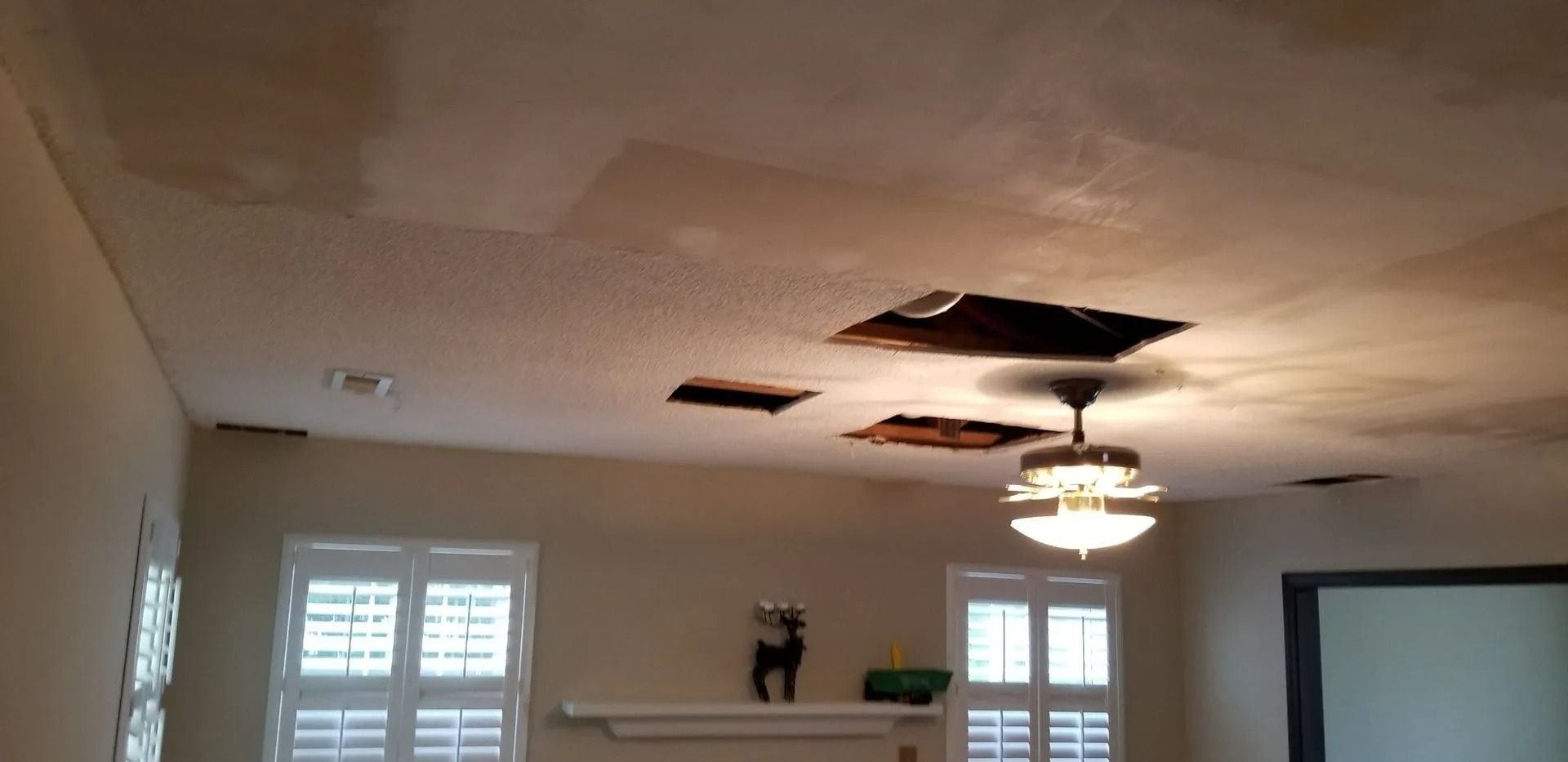 Living room ceiling with water damage and a hole near a lit ceiling fan