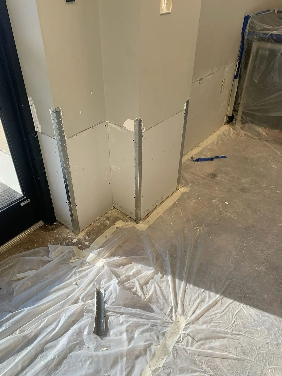 Interior wall corner with plastic floor covering, exposed trim, and construction debris on the floor