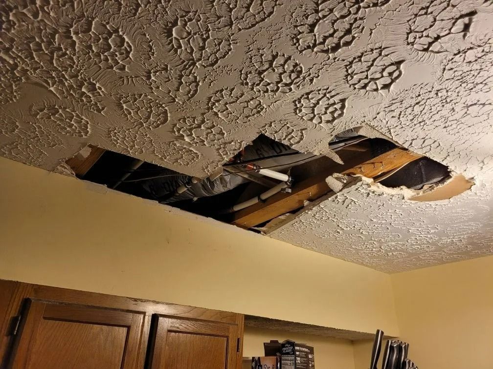 Damaged ceiling with large hole and fallen drywall above wooden kitchen cabinets