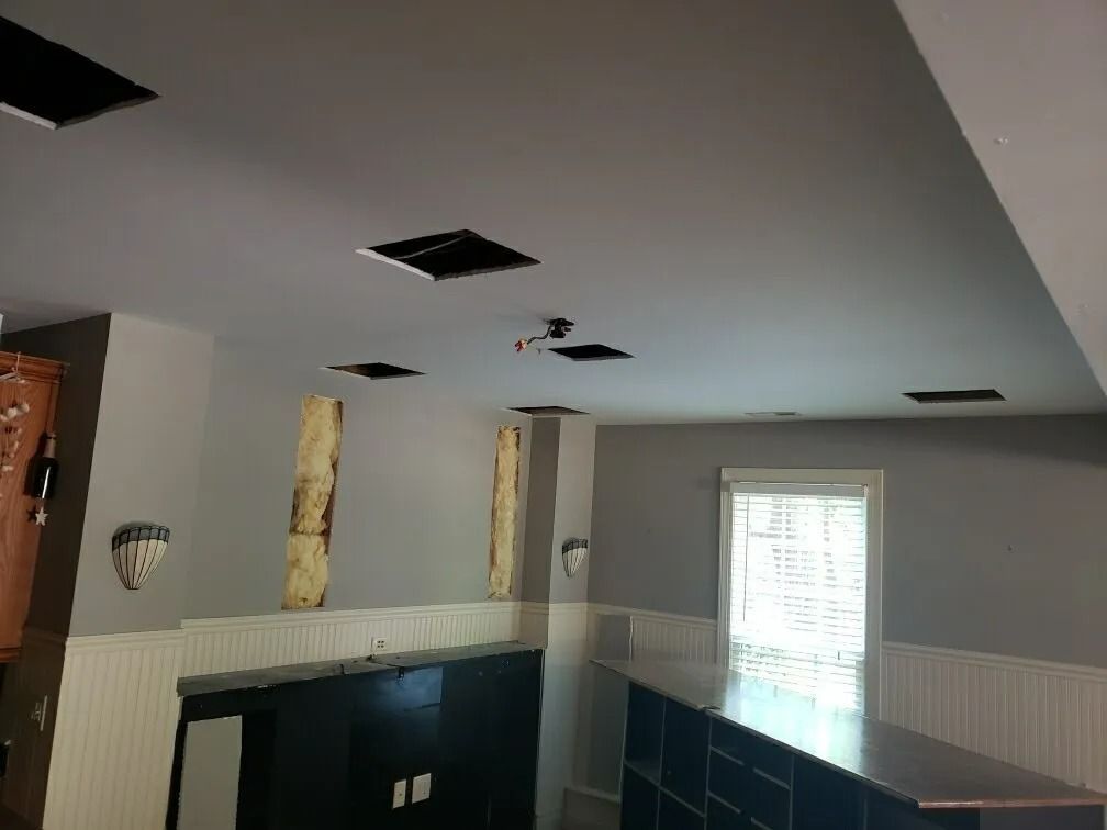 Interior room with damaged ceiling tiles and exposed holes above a stairwell.
