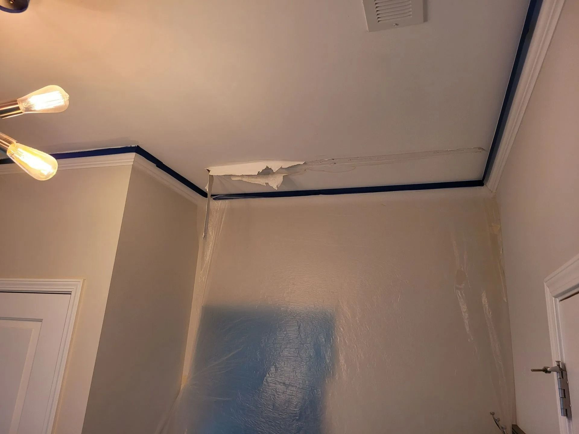 Bathroom corner with freshly painted gray walls, blue painter’s tape, and patching on the ceiling trim.