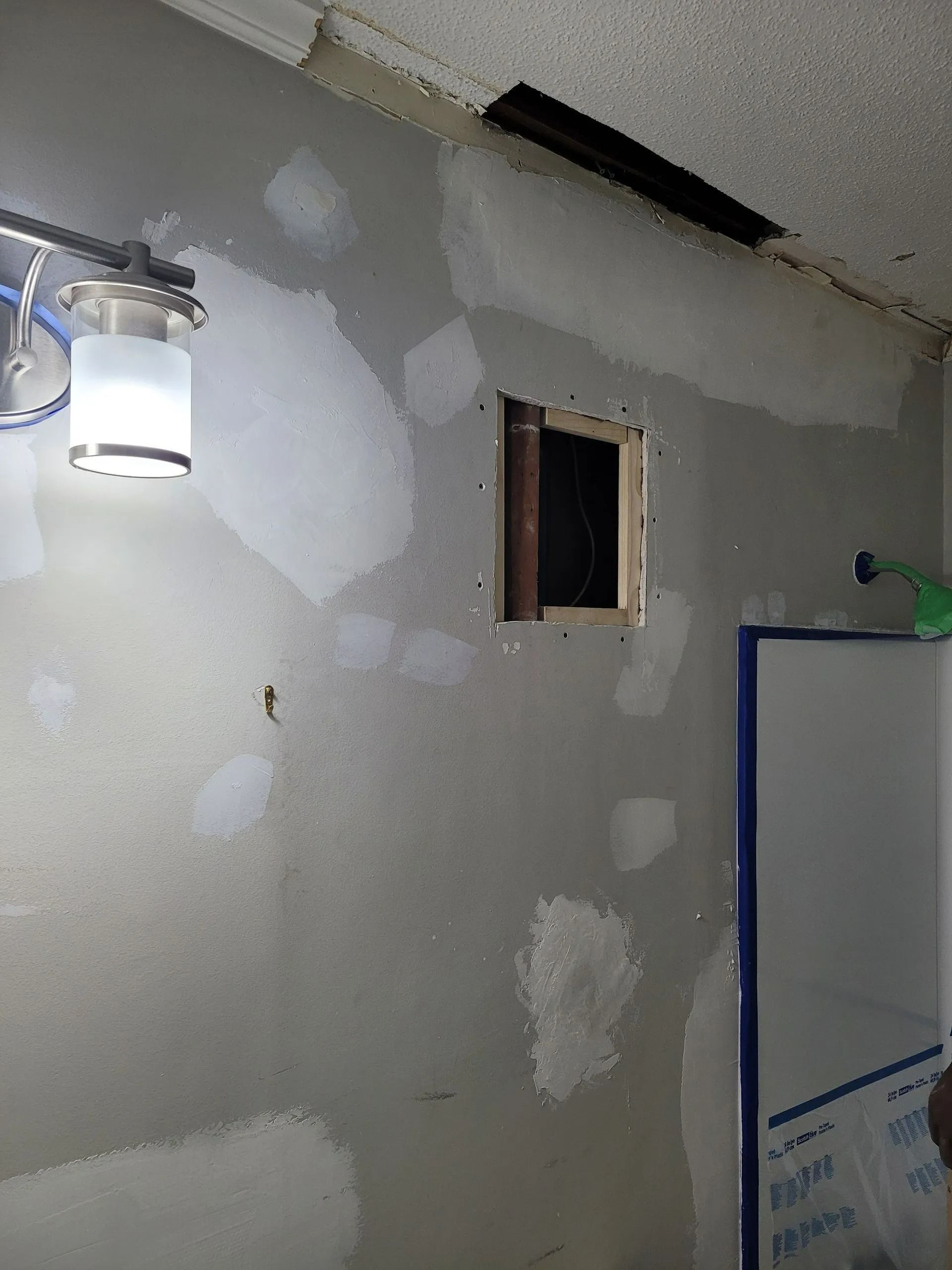 Partially finished room wall with patches, a small window, and a ceiling light.