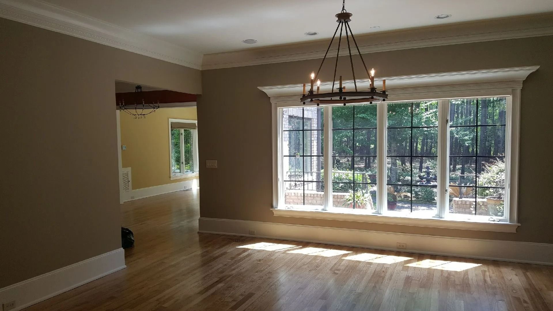 Empty living room with tan walls, hardwood floors, and a large windowed door under a chandelier.