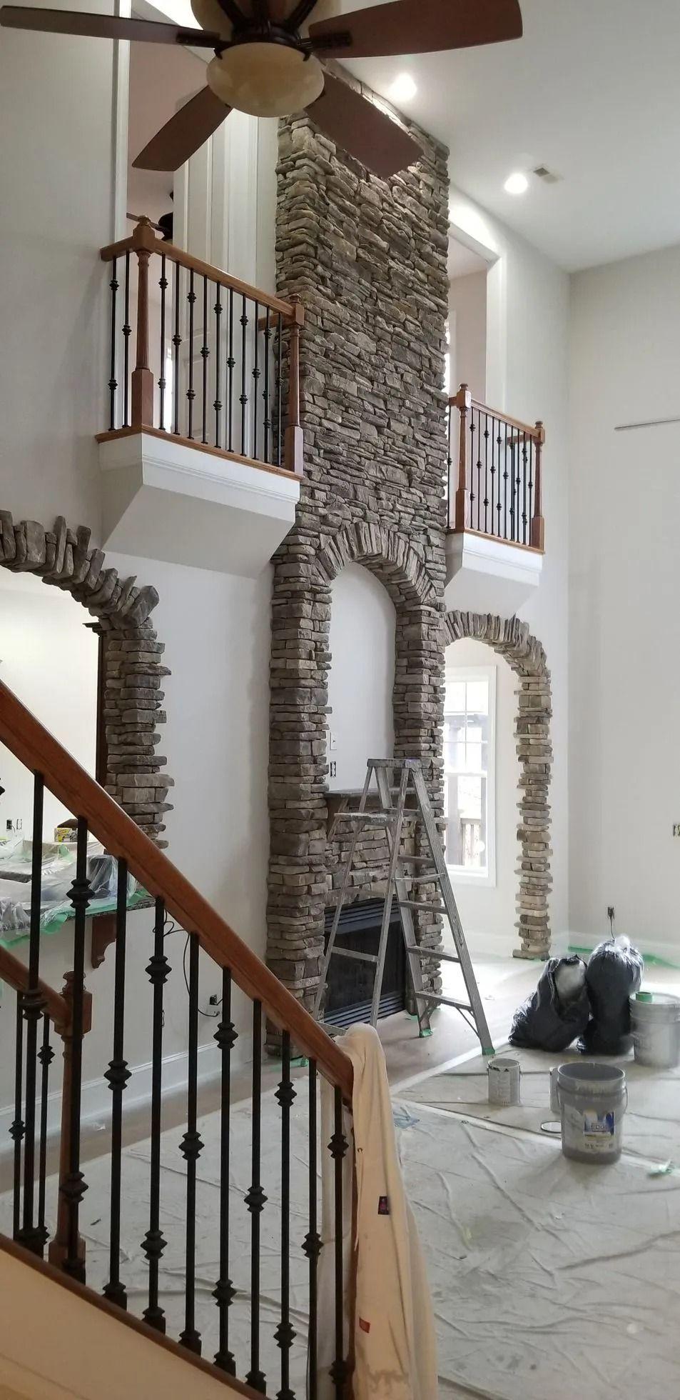 Bright foyer with stone fireplace, wood staircase, and ceiling fan under construction with plastic-covered floor.