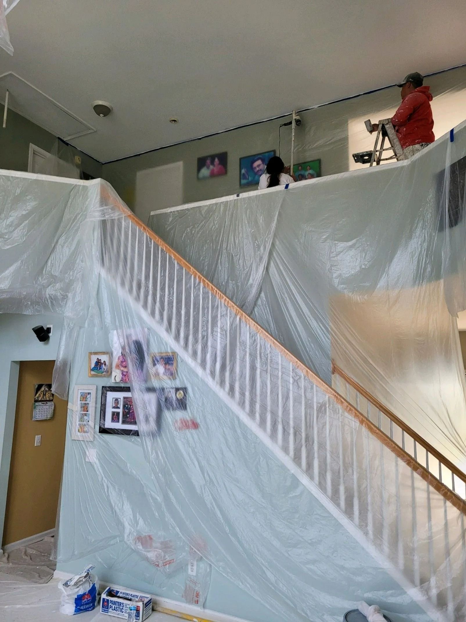 Indoor stairwell covered in plastic sheeting, with a person in red working on the upper landing