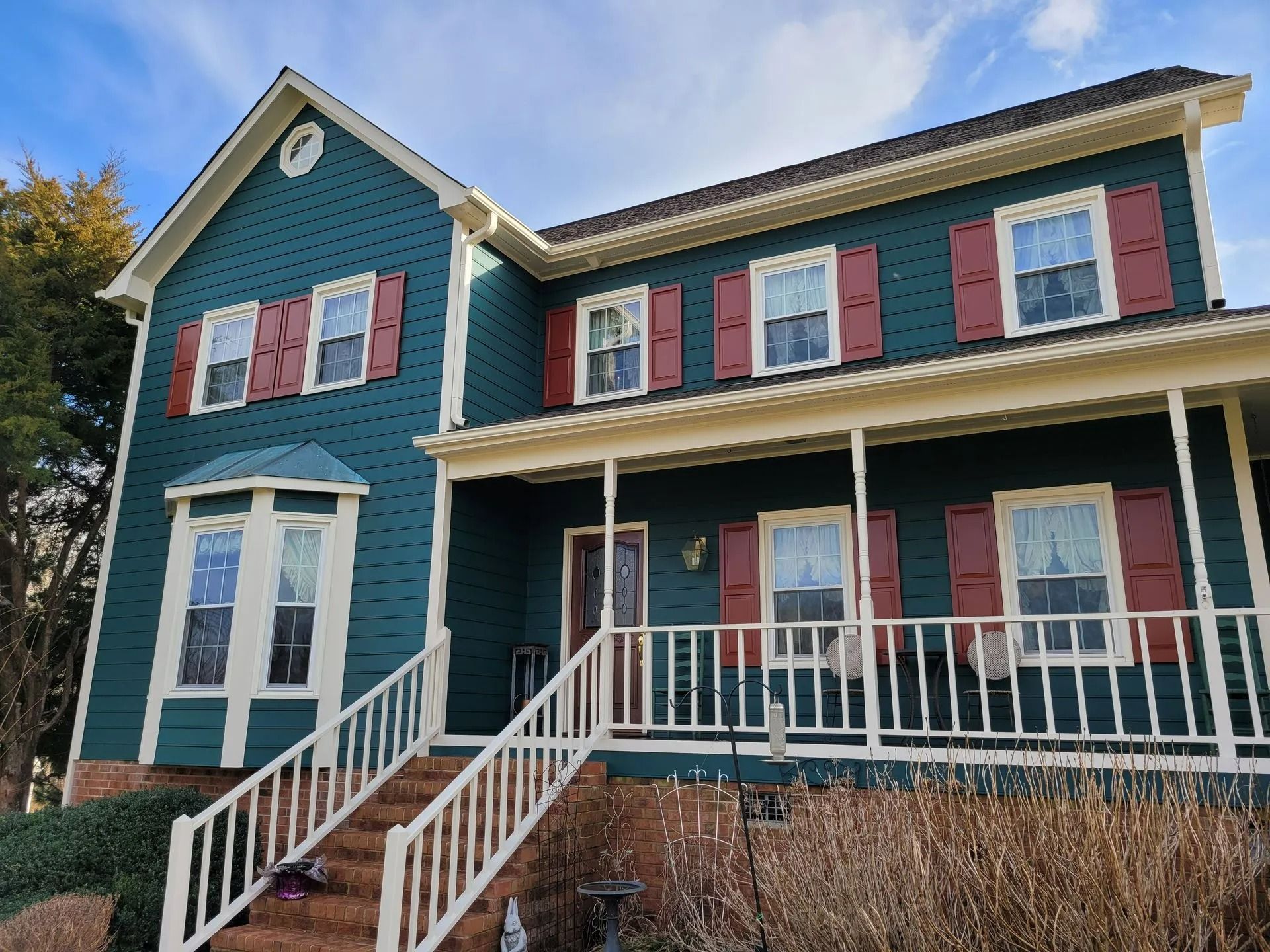 Teal house with red shutters and a white porch and railings under a cloudy sky