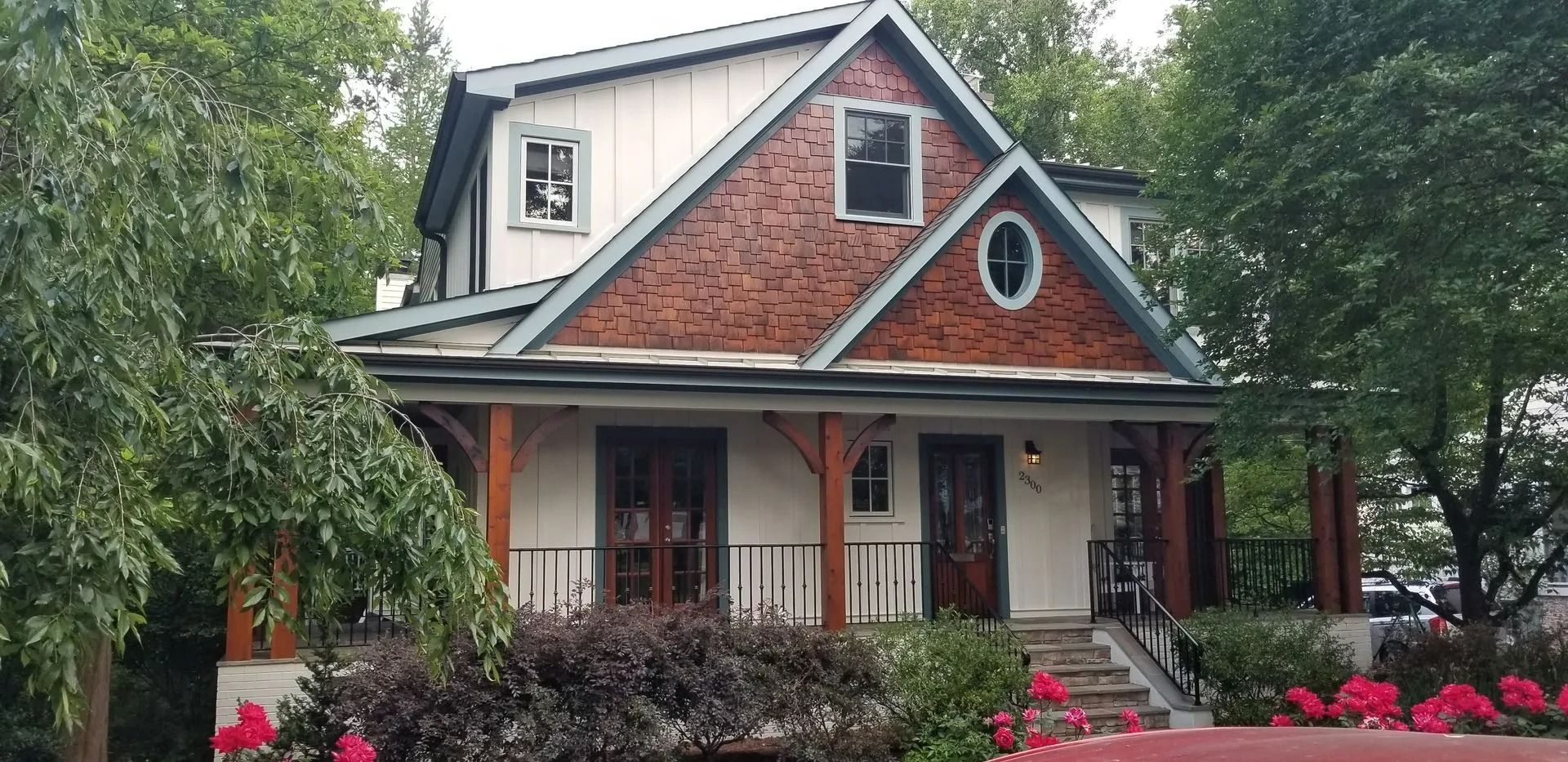 Charming brick-and-wood cottage with porch, gabled roof, and pink flowers in a leafy yard