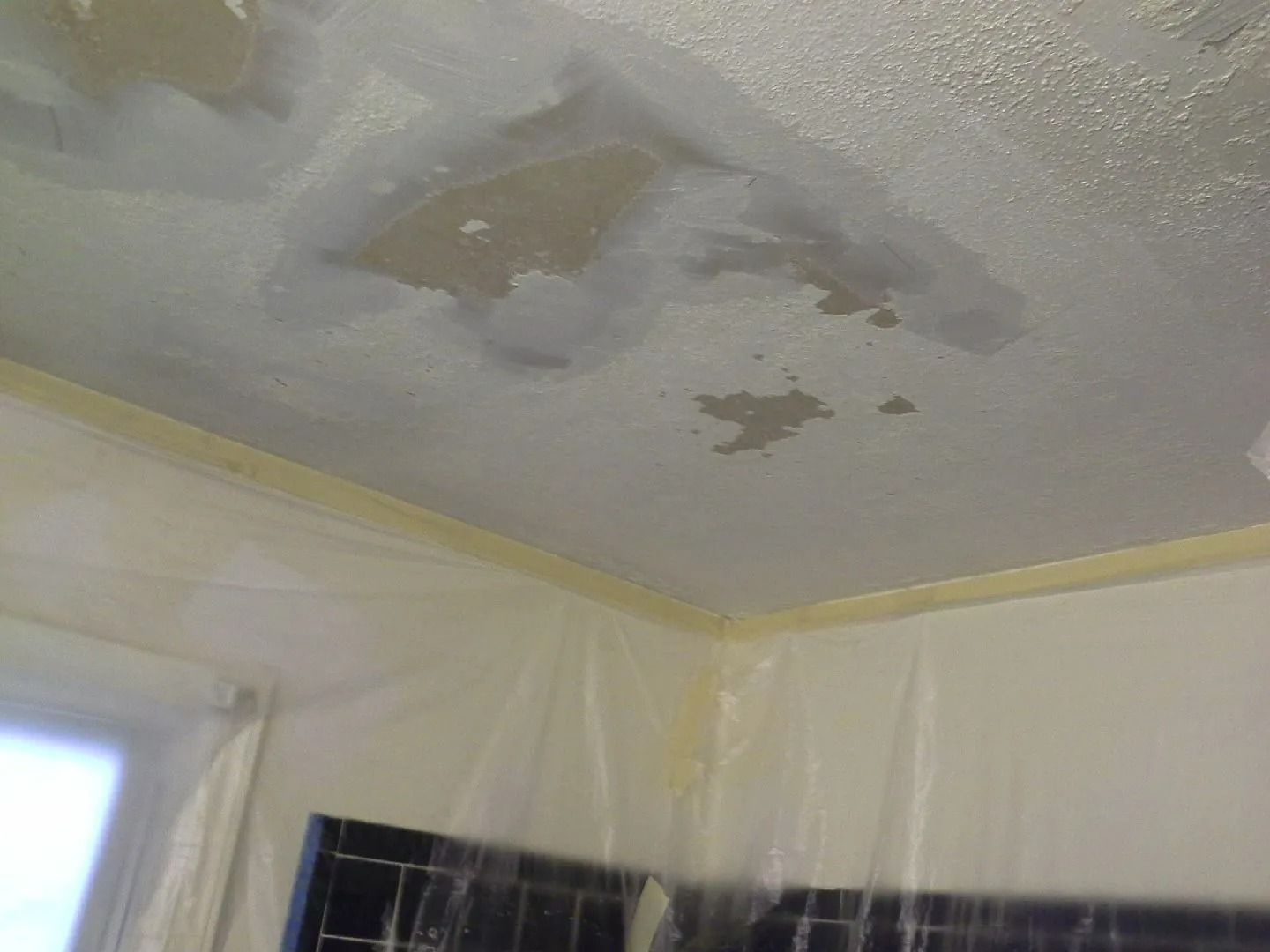 Water-stained ceiling with peeling paint above a room corner and window.