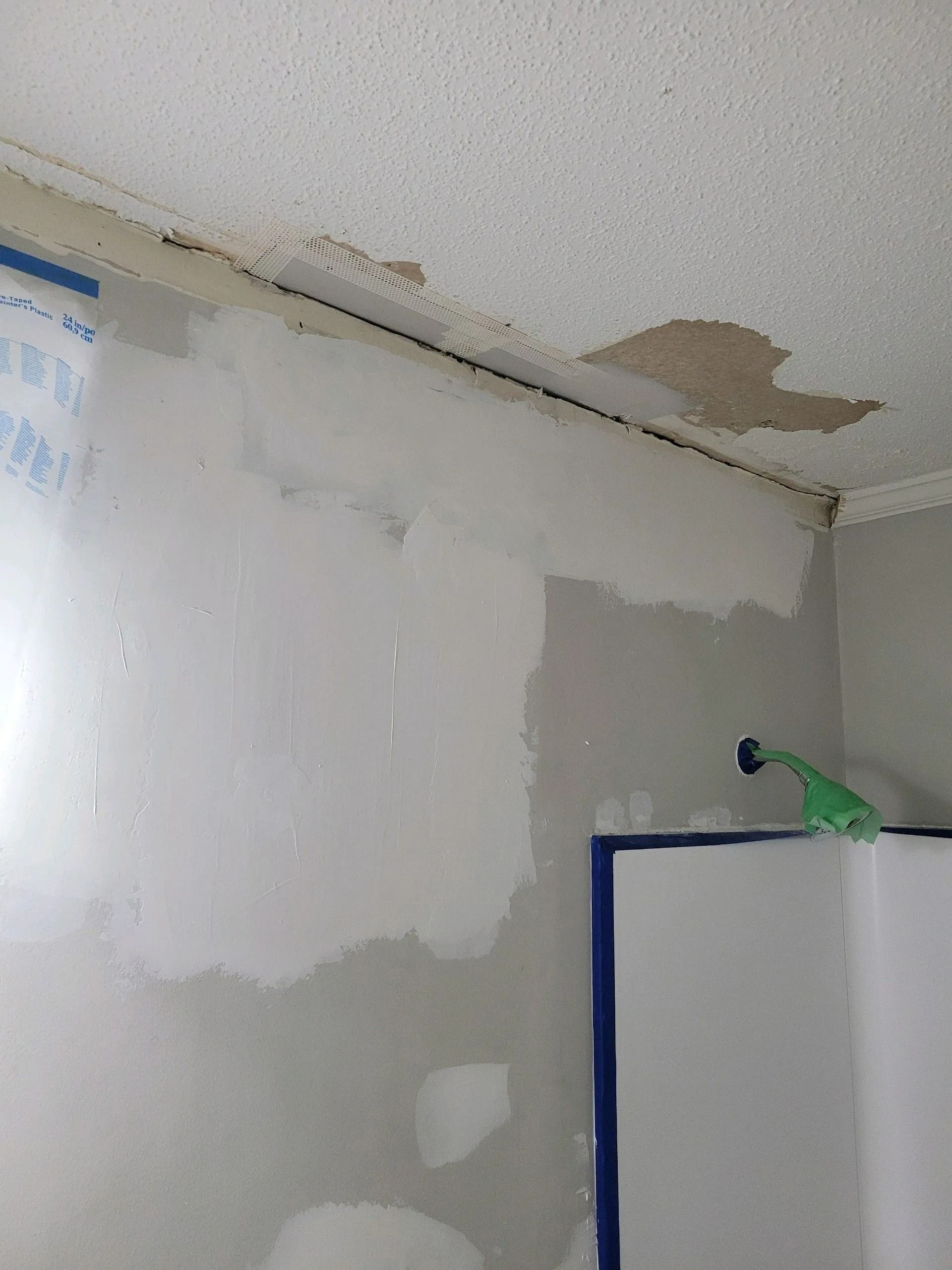 Peeling ceiling and water-damaged wall in a room with a white appliance and green bottle on top