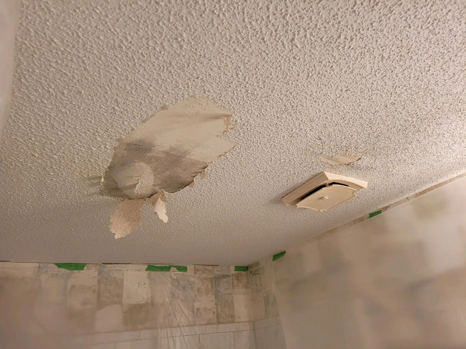Water-damaged bathroom ceiling with a large peeled patch and a vent nearby