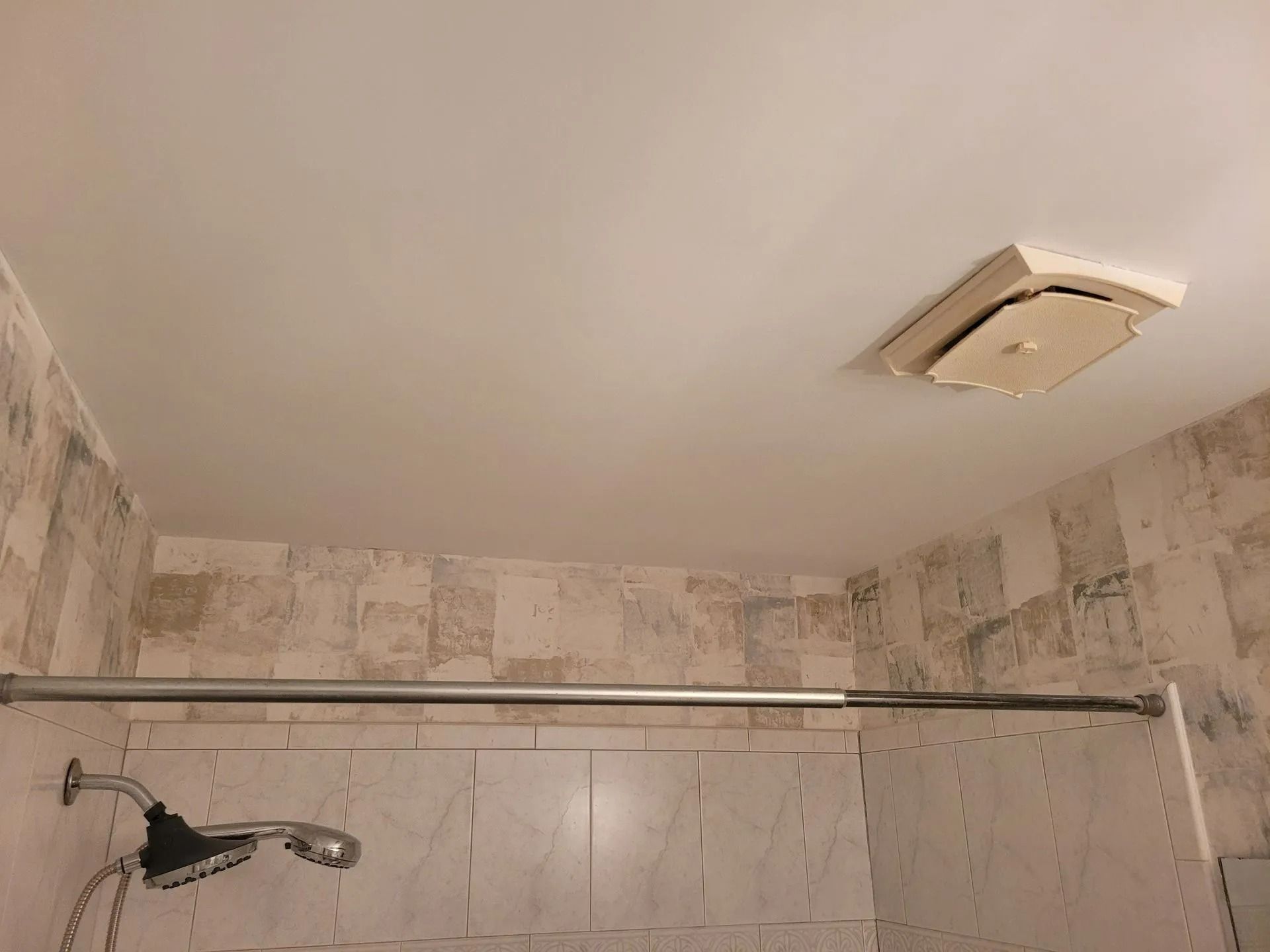 Small bathroom shower with tiled walls, ceiling vent, and chrome shower rod.