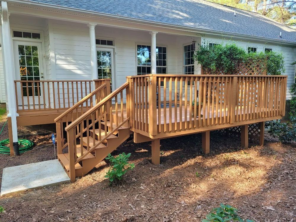 Wooden accessible deck ramp with stairs beside a house, surrounded by mulch and trees.