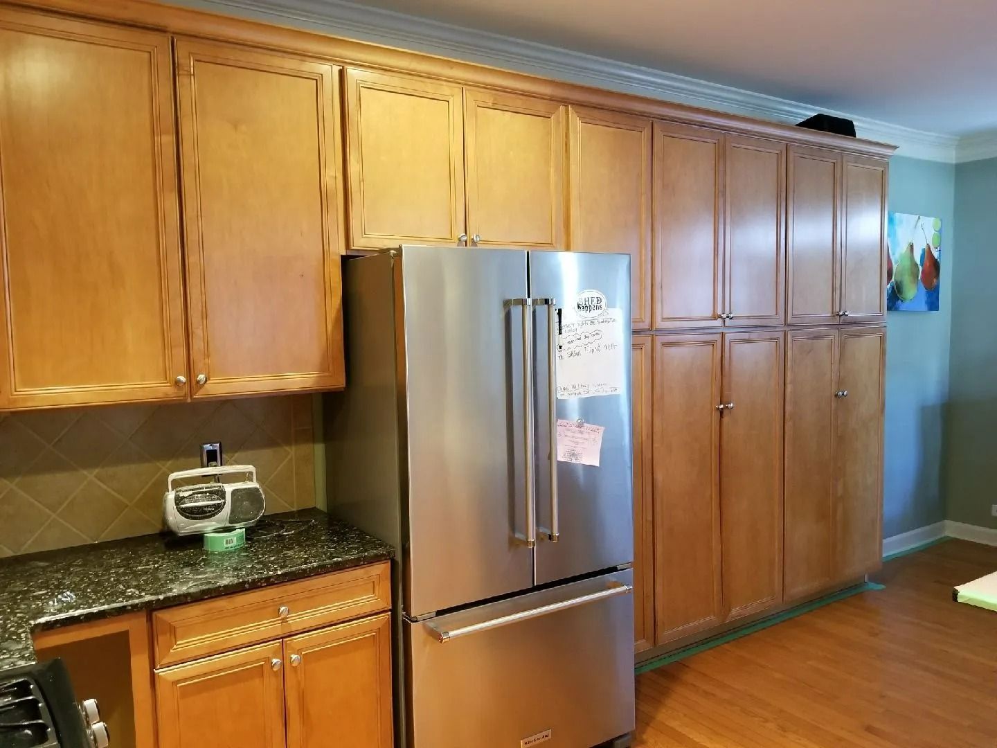Kitchen with stainless steel refrigerator, light wood cabinets, and dark granite countertops