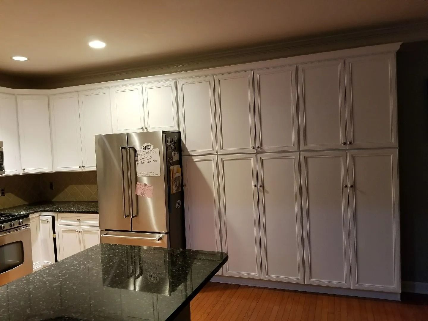 Kitchen with white cabinets, stainless steel refrigerator, and dark granite island countertop