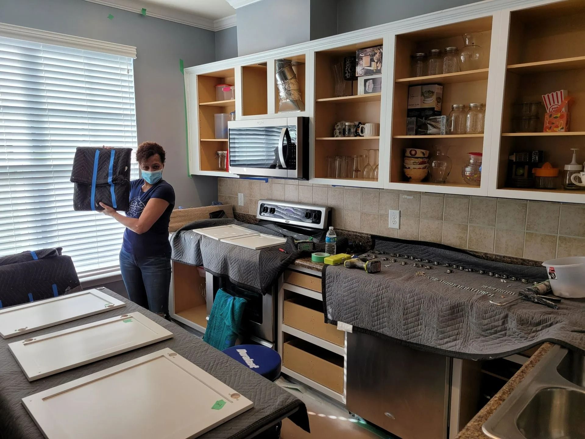 Kitchen with open cabinets, countertops, and a person cleaning near a window in a home interior.