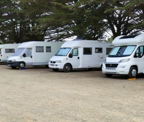 White recreational vehicles parked in a gravel lot under trees.