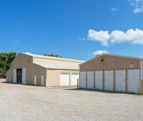 Row of white, closed storage unit doors with beige building and blue sky.