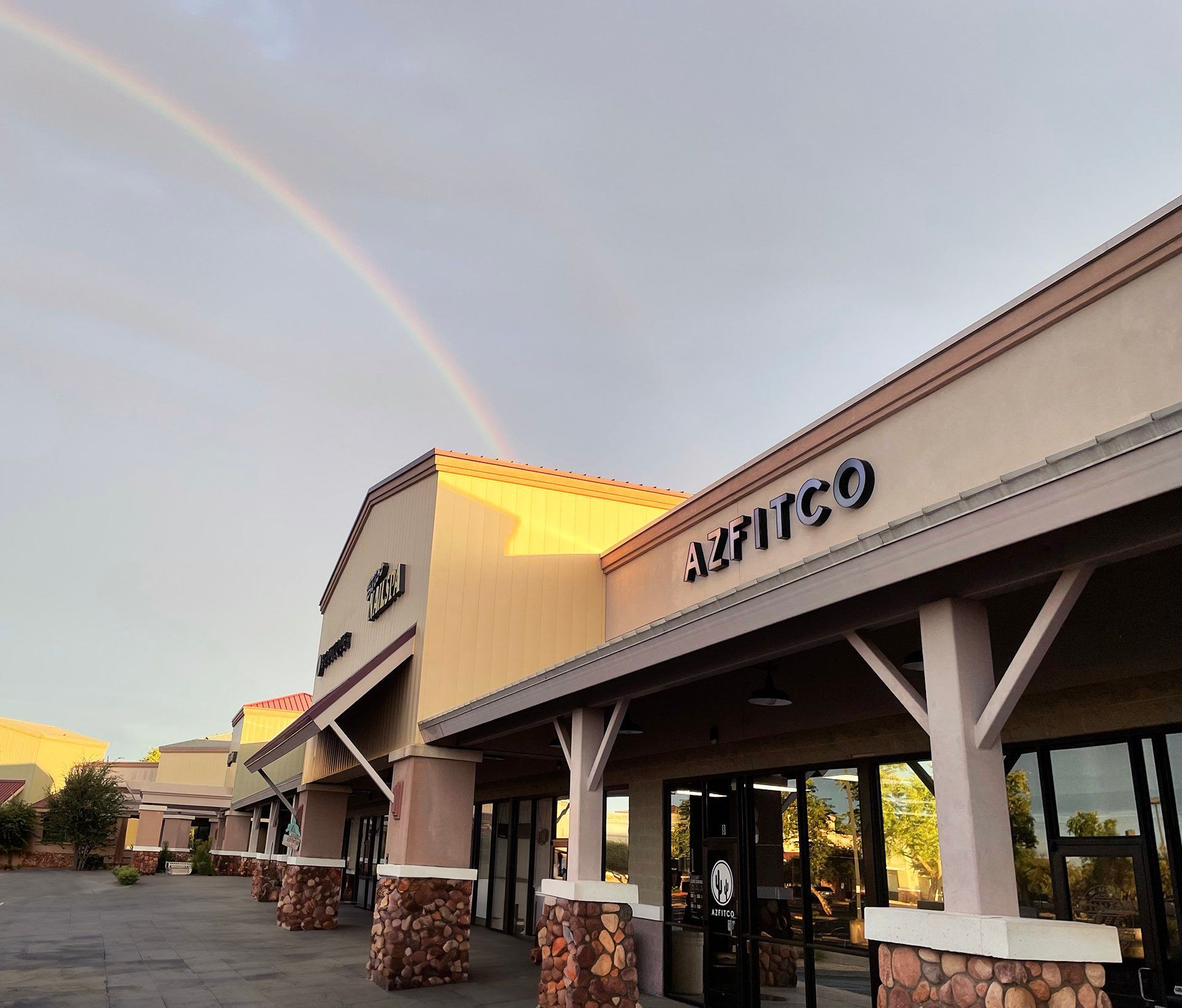 Strip mall storefronts at sunset with a rainbow arcing overhead
