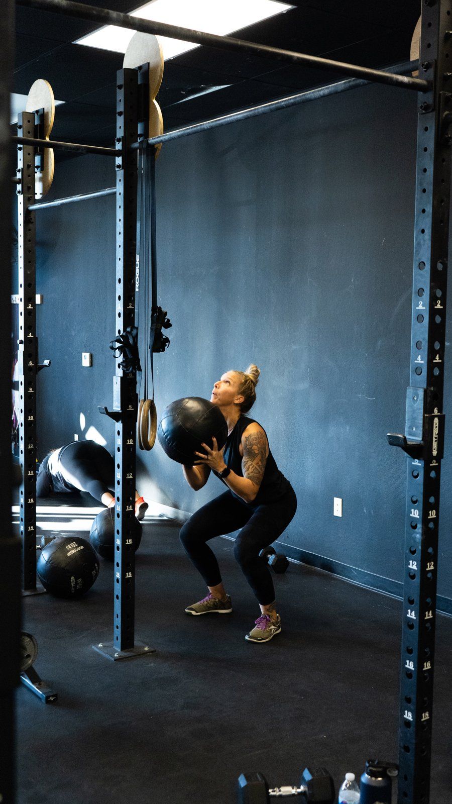 Woman doing a medicine ball squat in AZFITCO, a gym in Chandler, AZ,with a squat rack and dark walls.