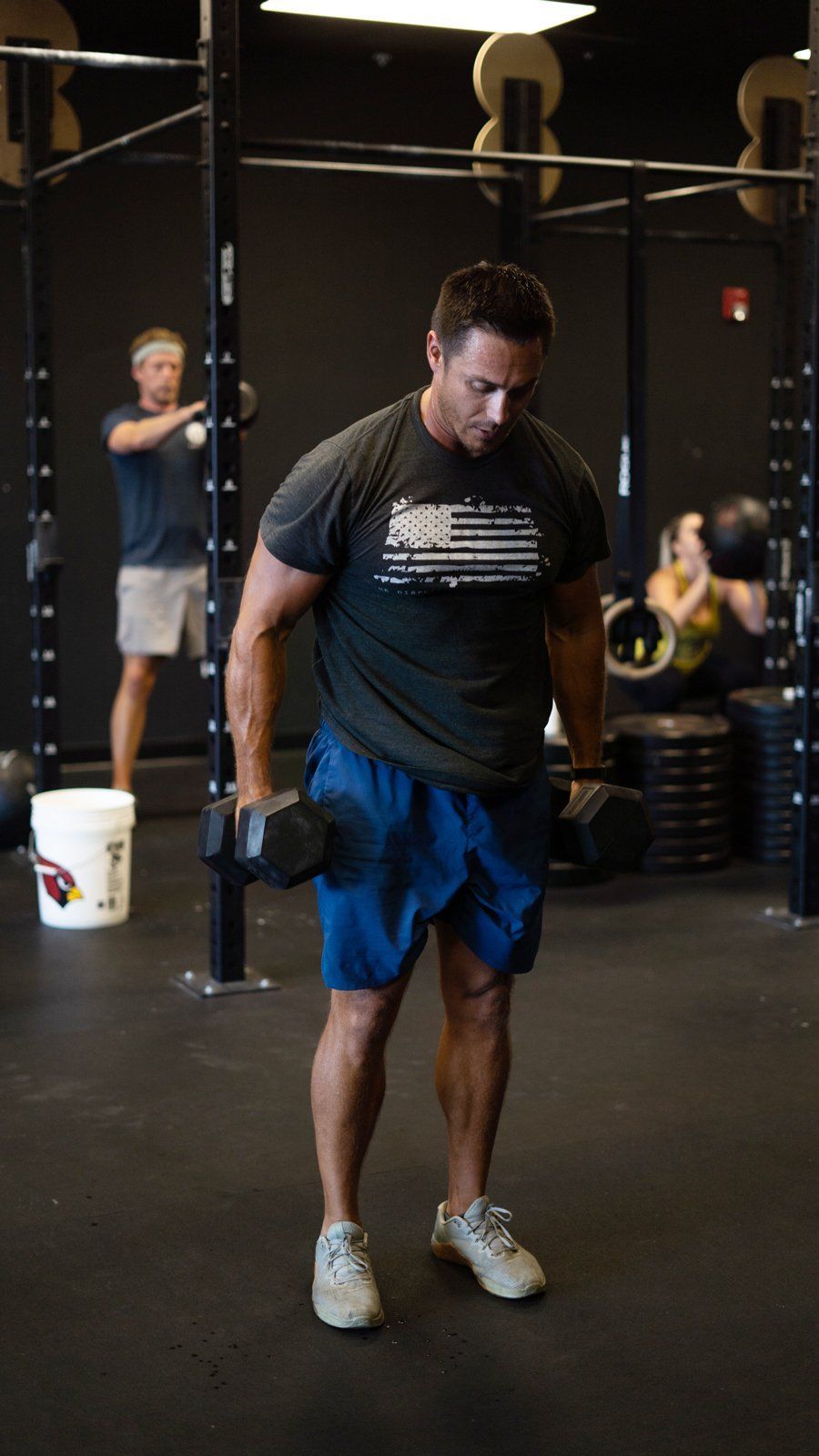 Man doing a dumbbell exercise at AZFITCO, a gym in Chandler, AZ, with other people working out in the background.