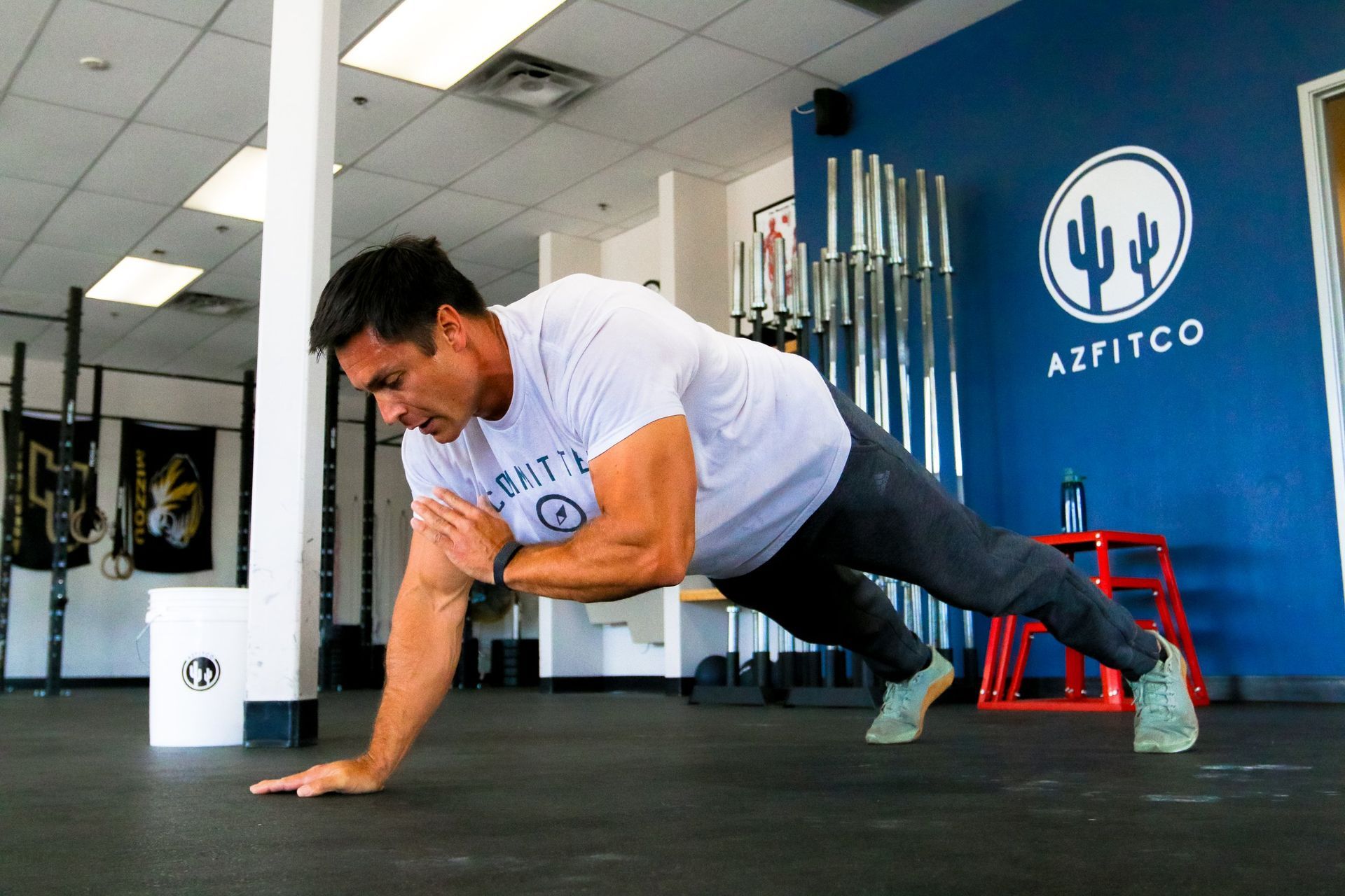 Man doing a plank exercise in AZFITCO, a gym in Chandler, AZ, with weighted bars and blue walls