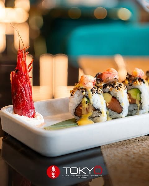 Rotolo di sushi e grande gambero rosso con salsa su un piatto bianco; è visibile il logo del ristorante 