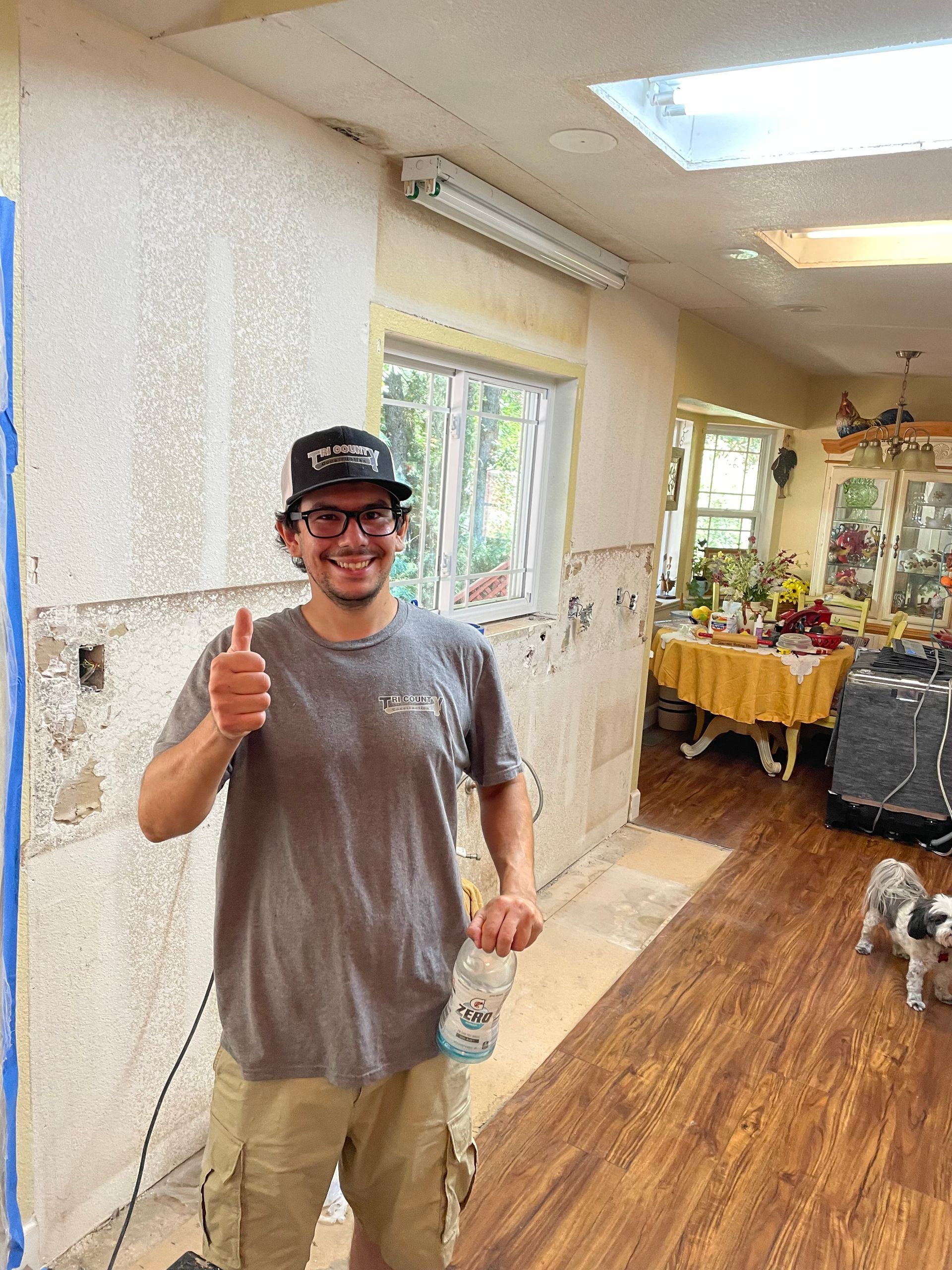 Man smiling and giving a thumbs-up in a bright room with wooden floors and plants