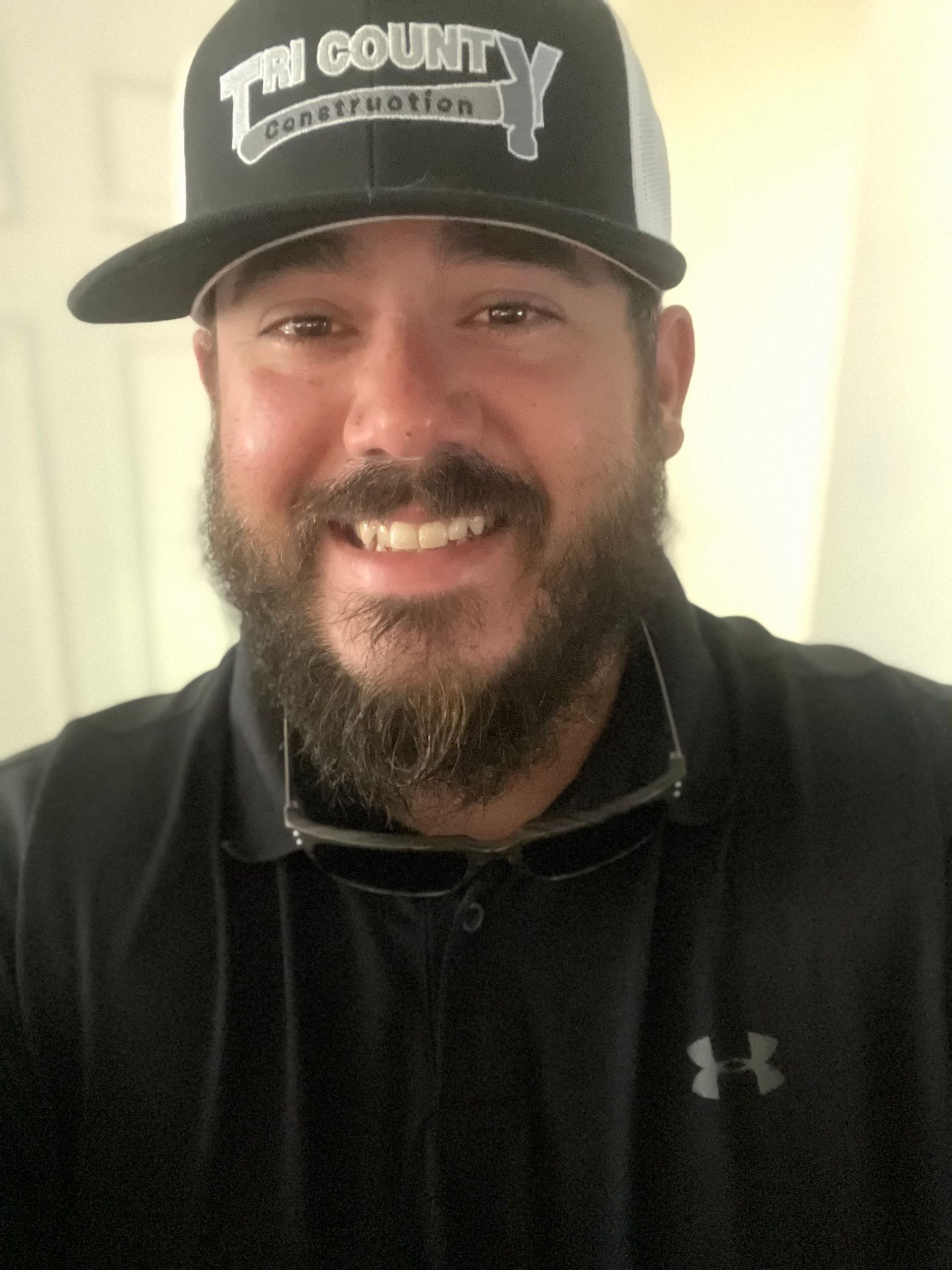 Smiling man in a black cap and black polo shirt against a light indoor wall