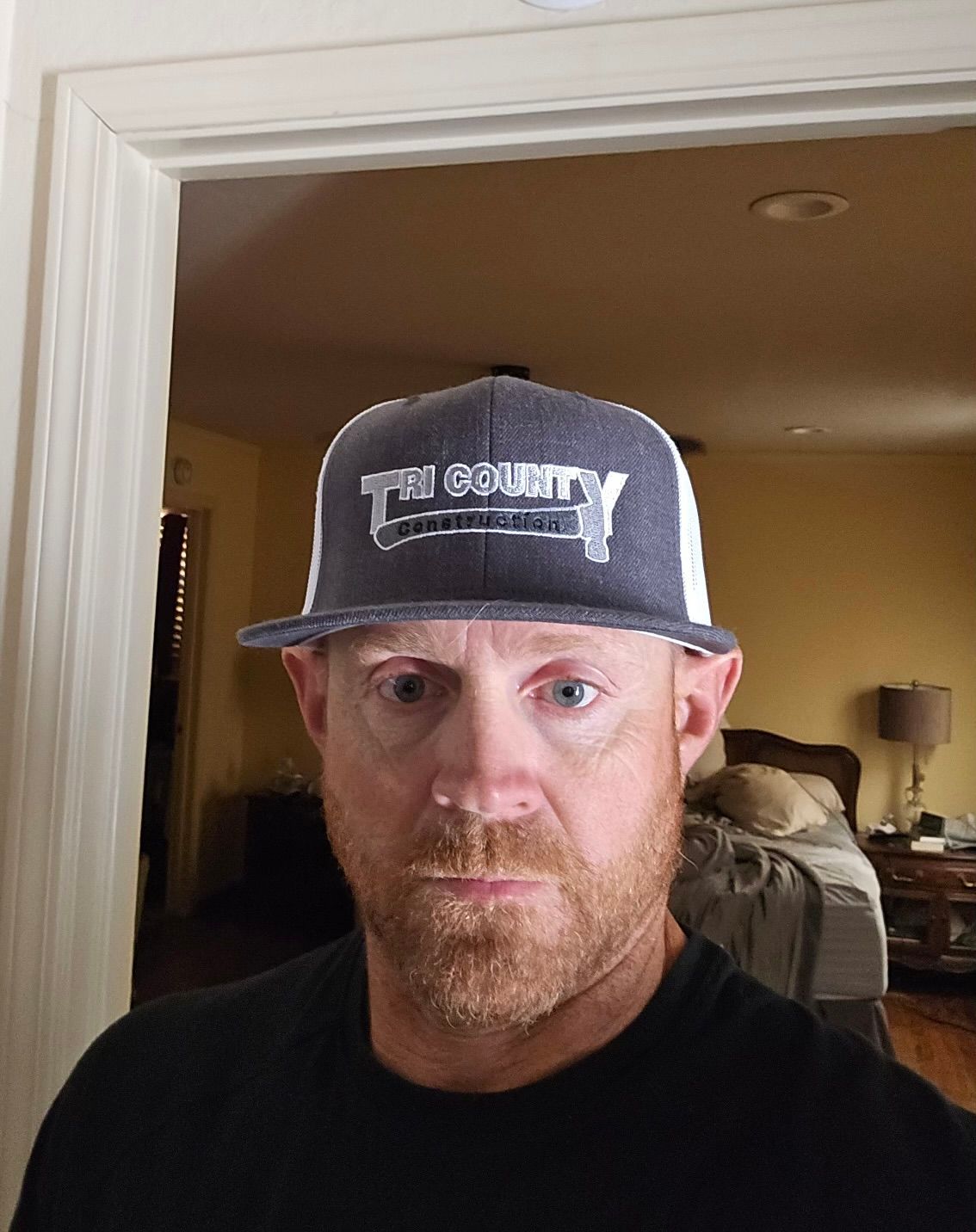 Man in a gray cap and black shirt, standing indoors in a doorway.