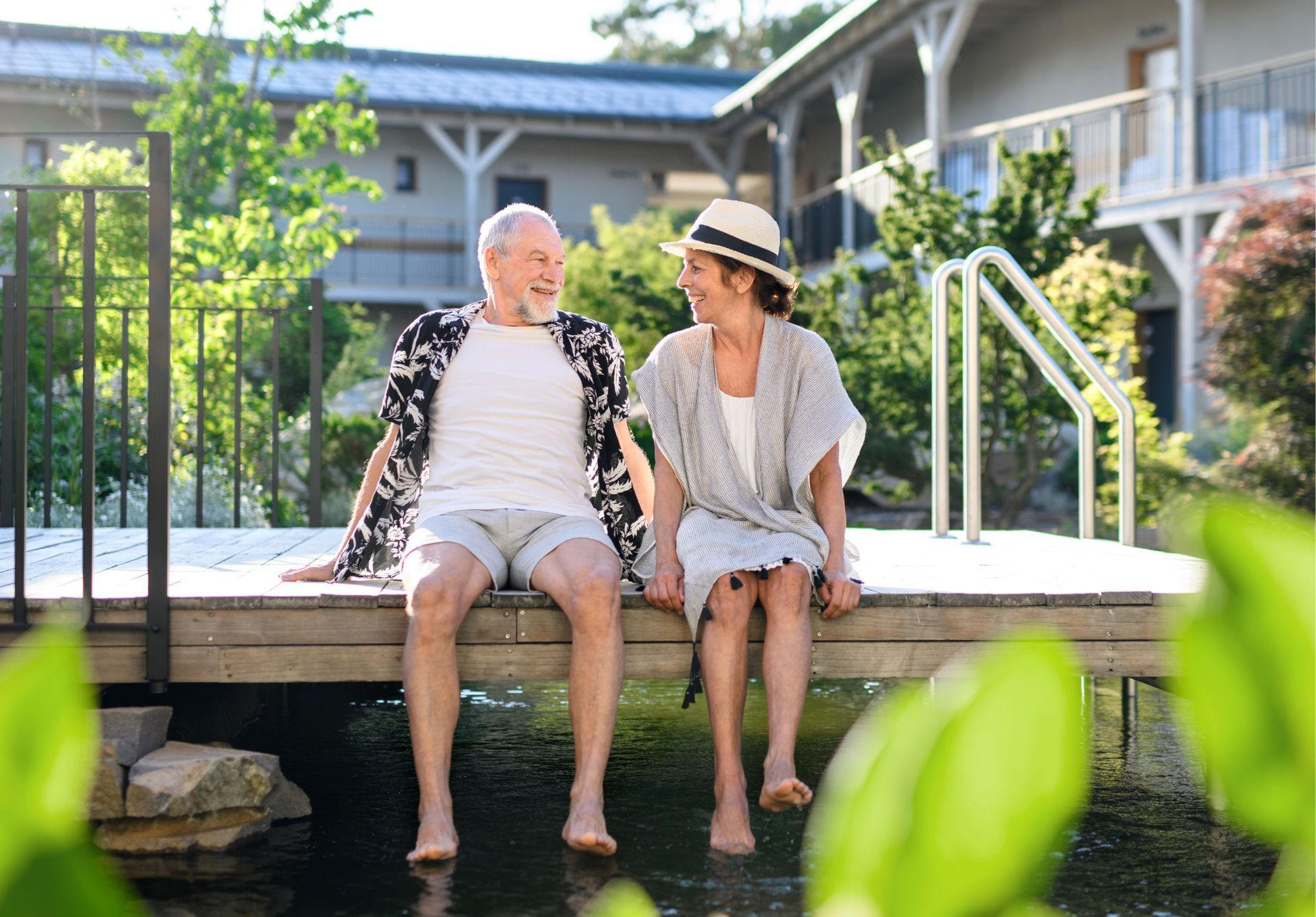 A man and a woman are sitting on a dock next to a pond.