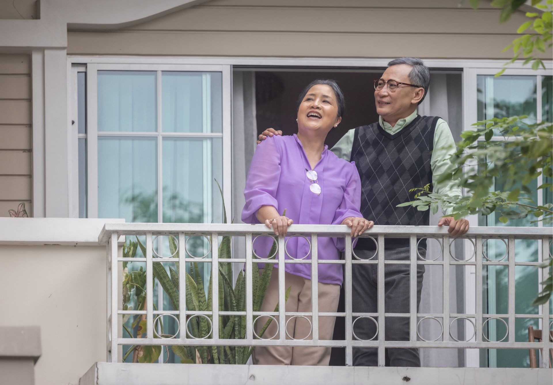 A man and a woman are standing on a balcony looking out of a window.