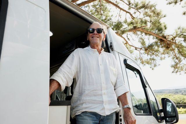 A man wearing sunglasses is standing in the doorway of a camper van.