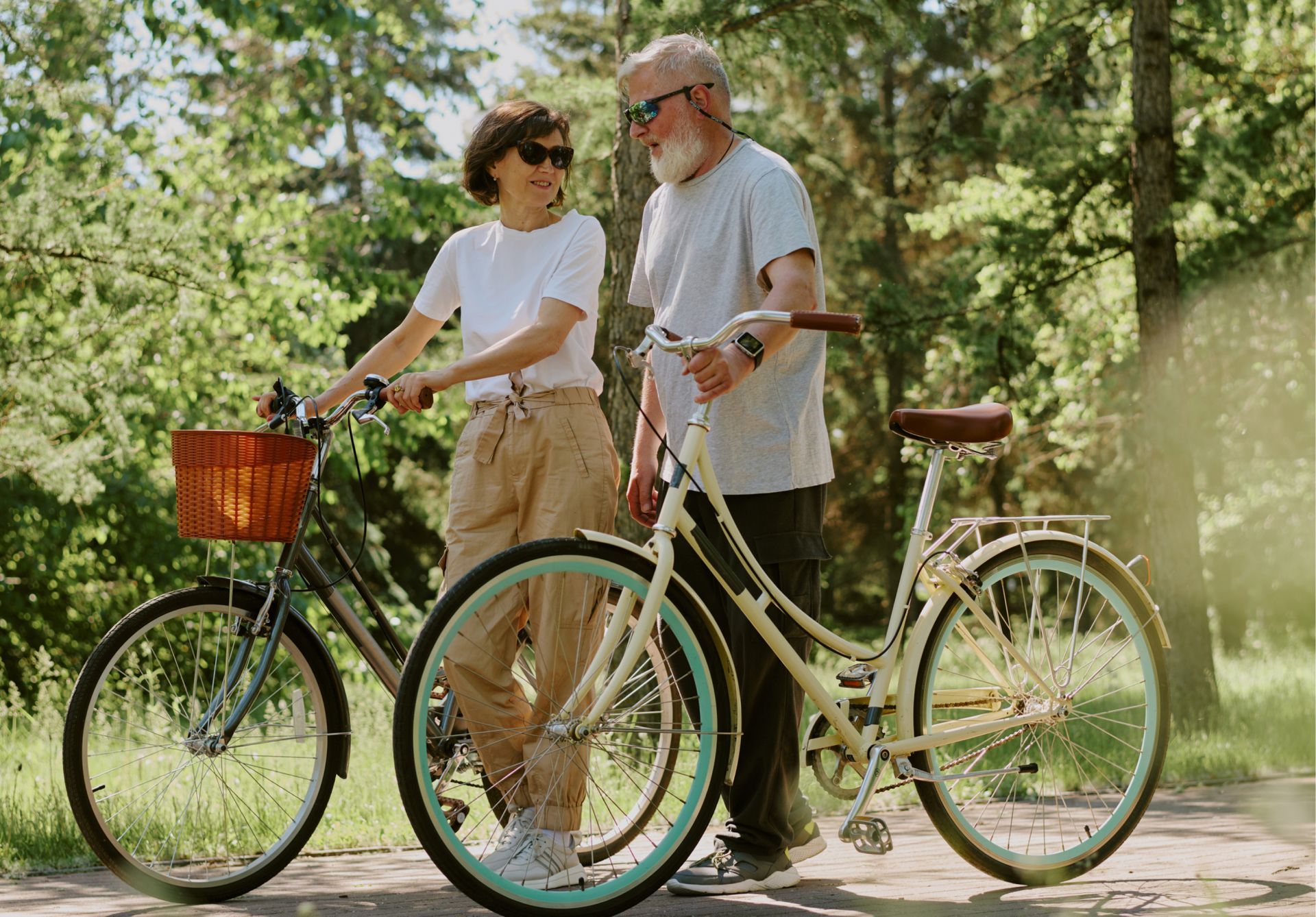 A man and a woman are standing next to bicycles in a park.