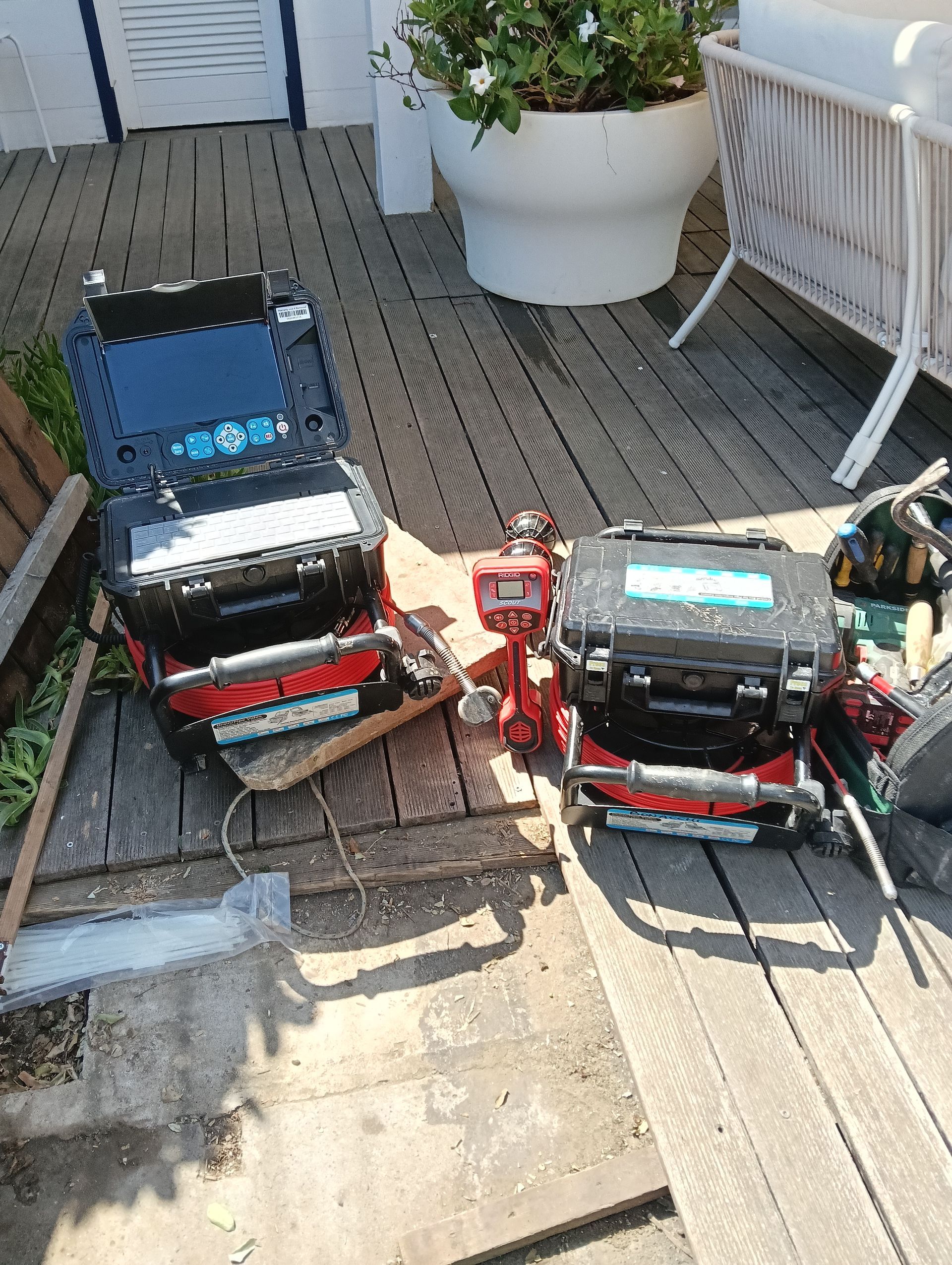 Due piccoli camioncini giocattolo su una piattaforma di legno, uno nero e uno rosso, accanto a una fioriera bianca e una panchina.