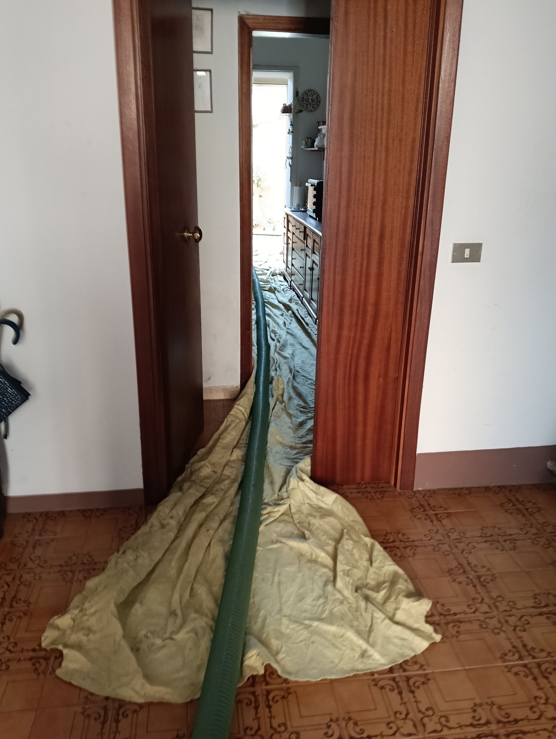 Un tubo verde si estendeva attraverso una porta, drappeggiato su un telo beige su un pavimento piastrellato.